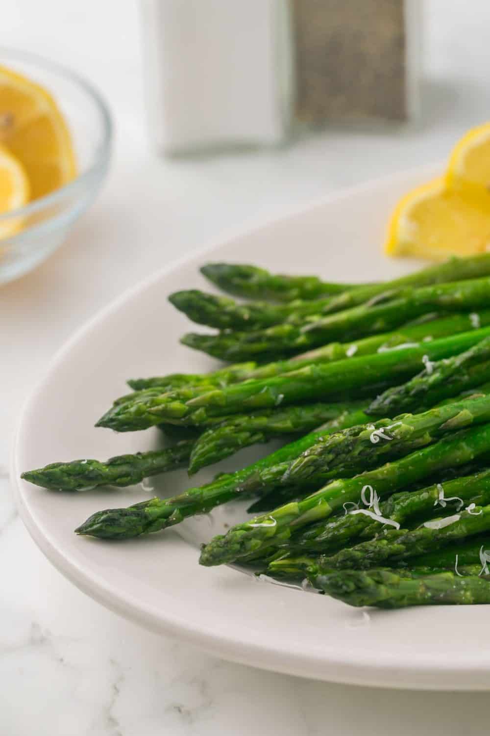 a white plate with sautéed asparagus with parmesan cheese and lemon on the side