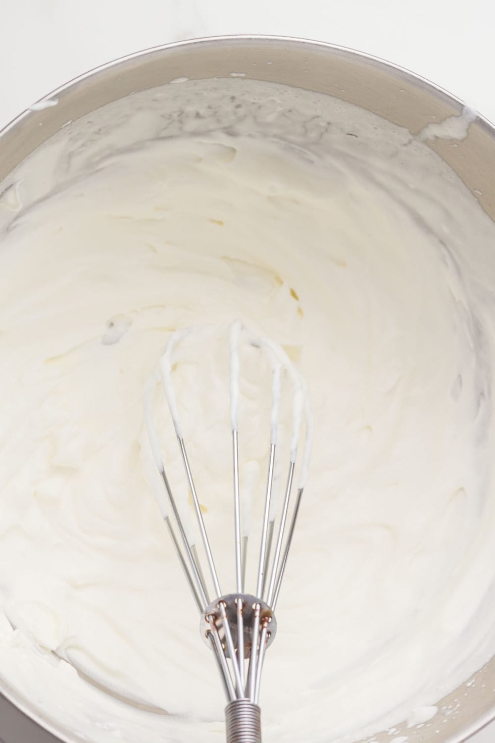 metal mixing bowl with whipping cream and a whisk inside