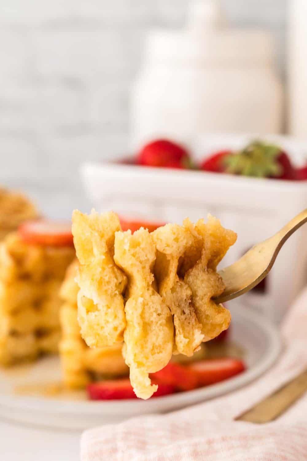 POV forkful of a stack of buttermilk waffles syrup and fresh strawberries.