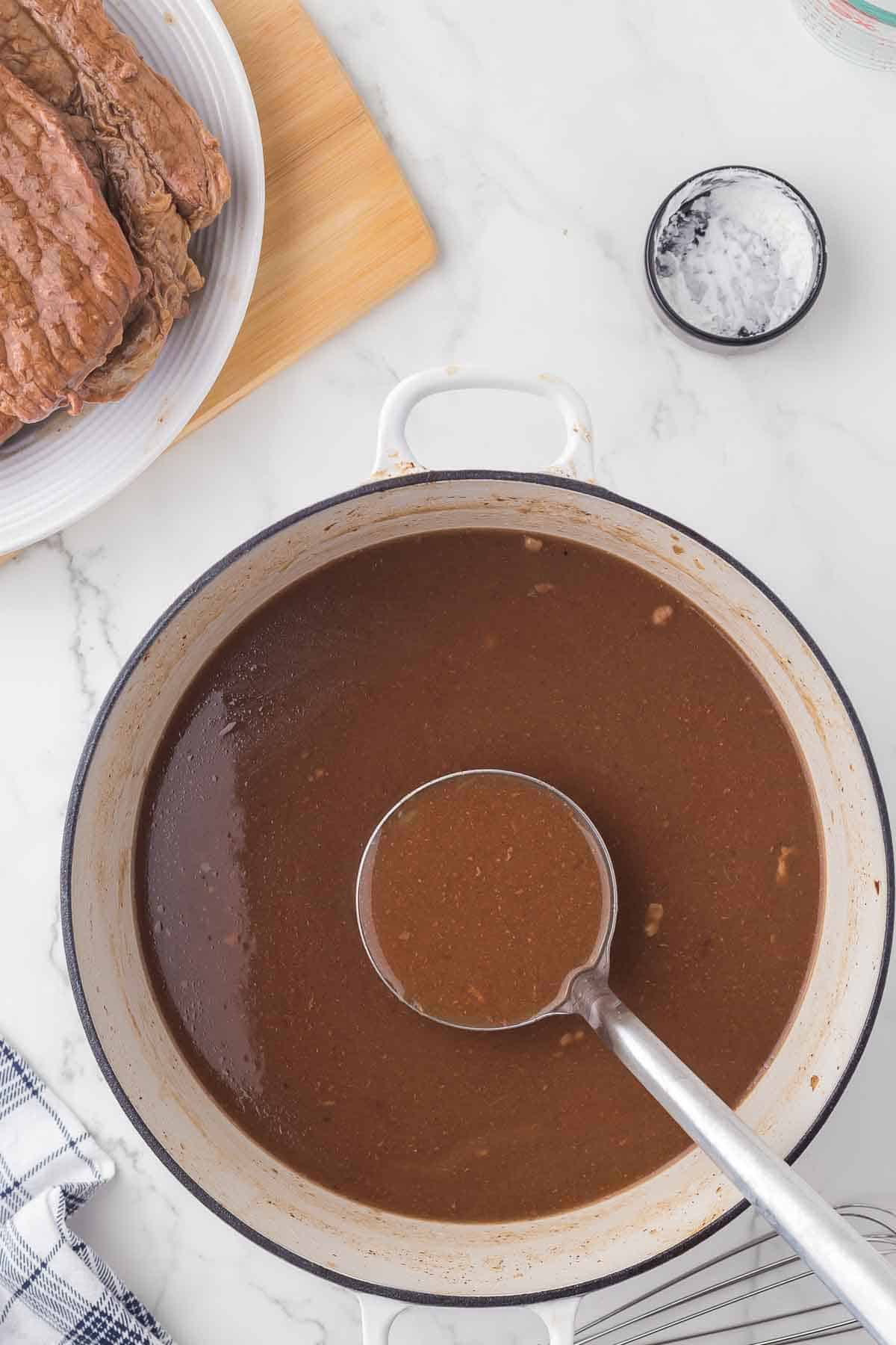 white dutch pot with liquid to make gravy and a ladle inside.