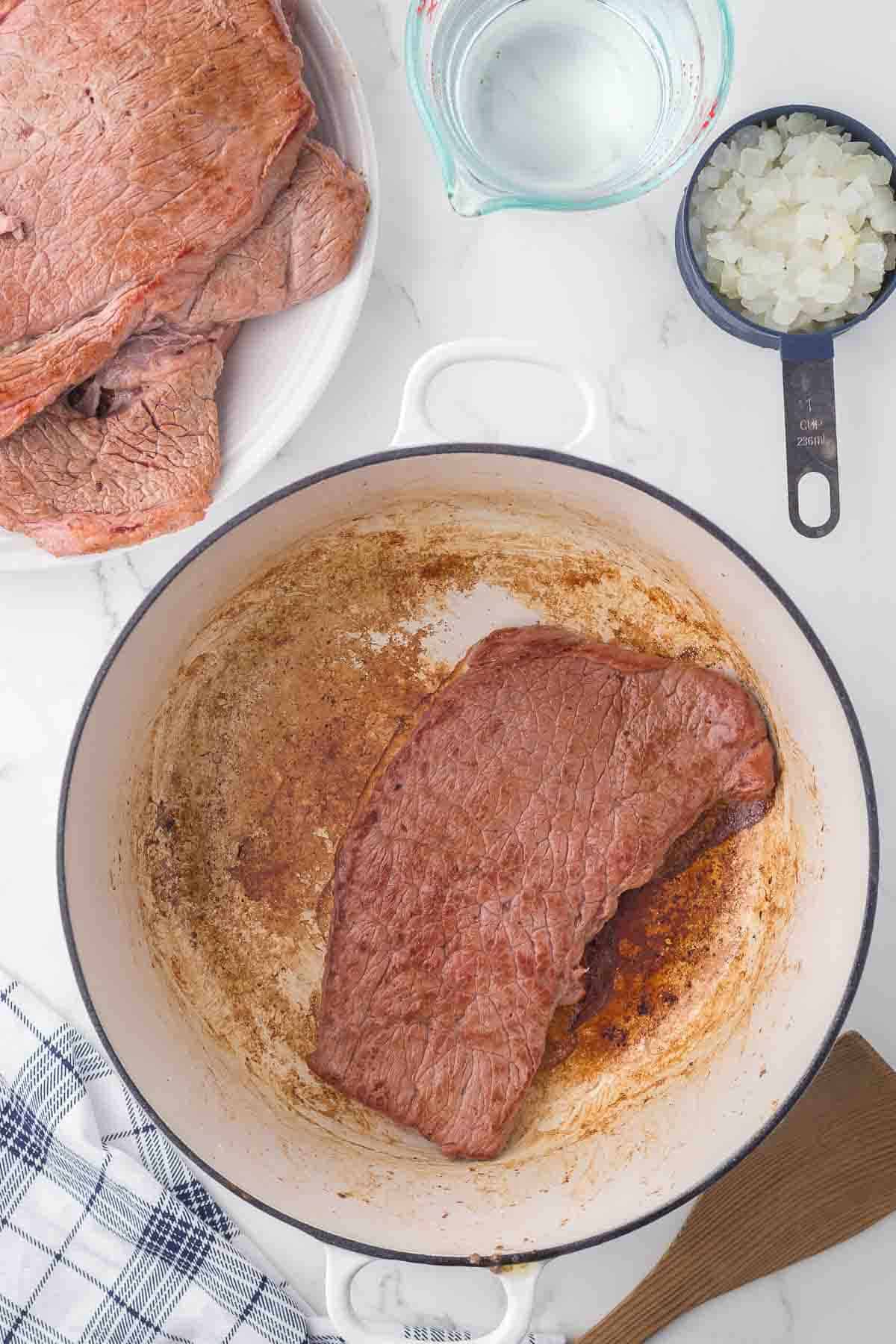 oiled pan with a round beef steak in progress of cooking.