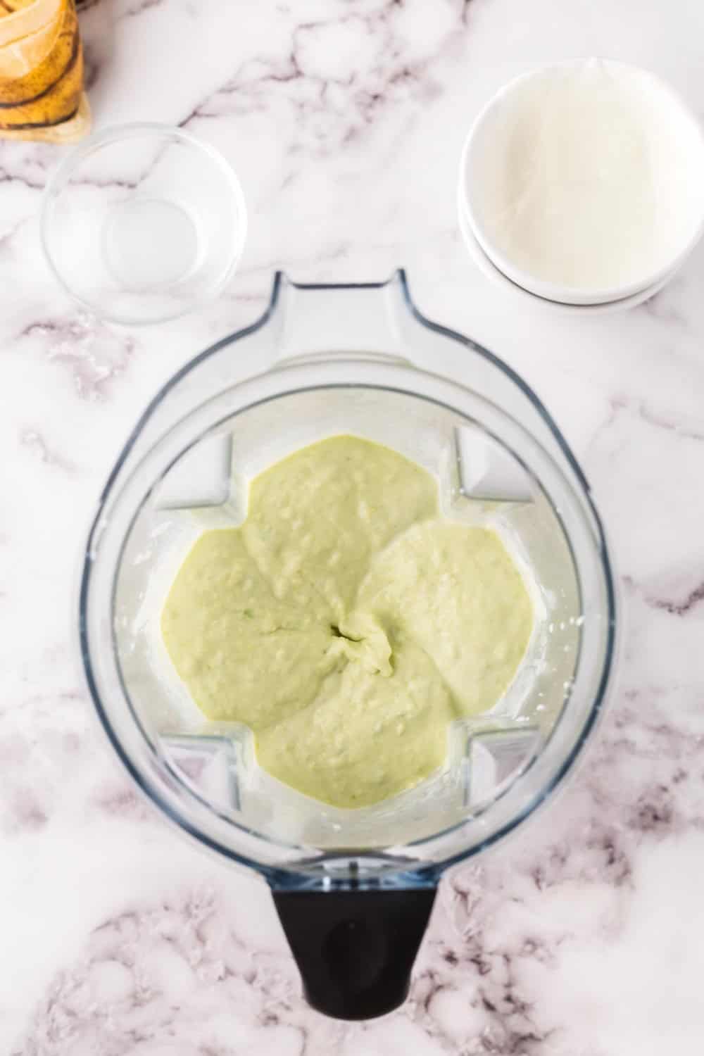 blender pitcher with raw ingredients for avocado smoothie blended smooth.