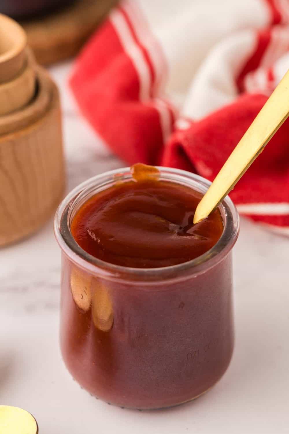 small glass jar with barbecue sauce and a golden spoon inside.