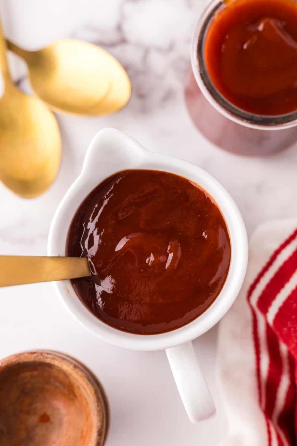 small white pitcher with barbecue sauce and a golden spoon inside.