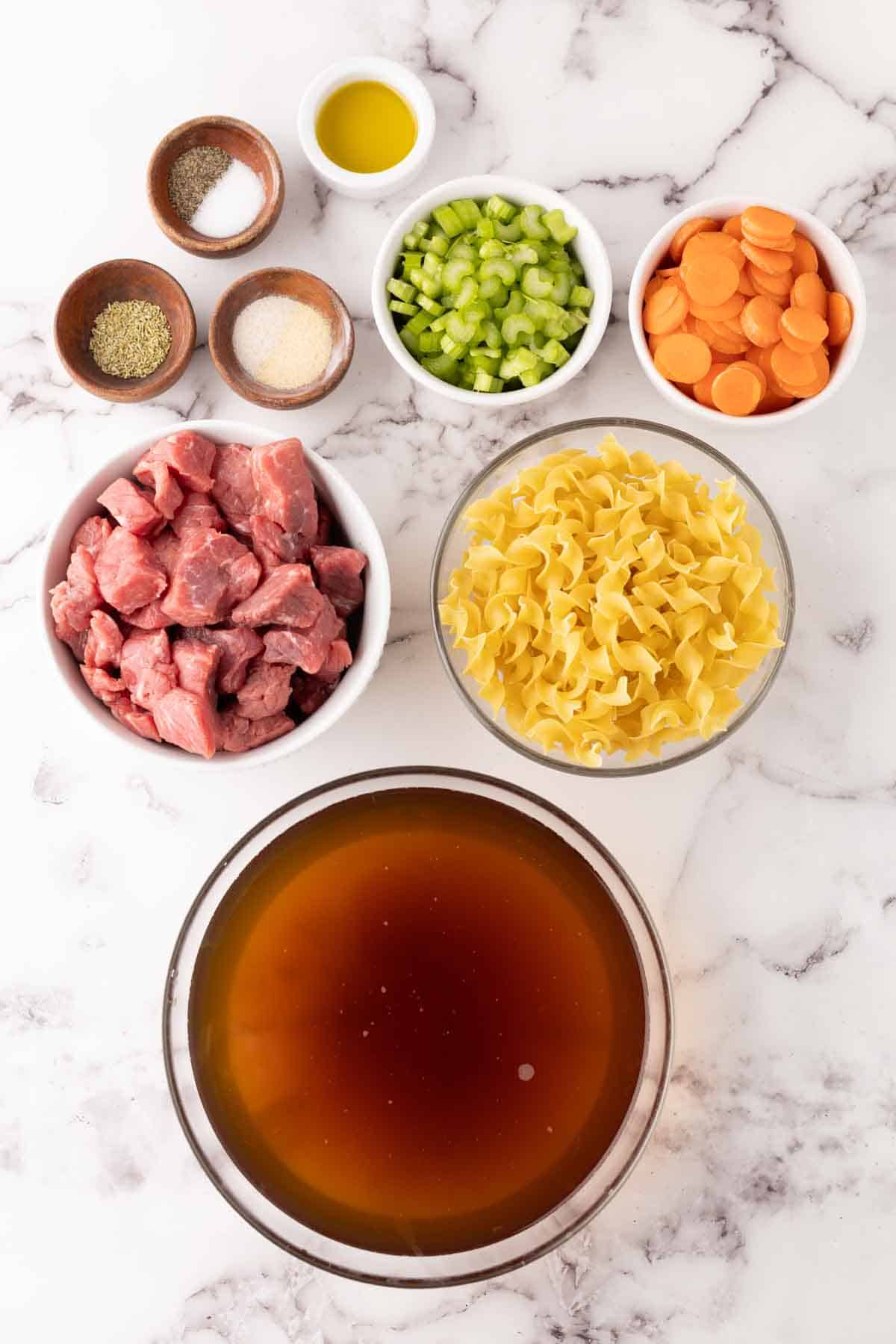 portion bowls each with raw ingredient to make beef noodle soup.