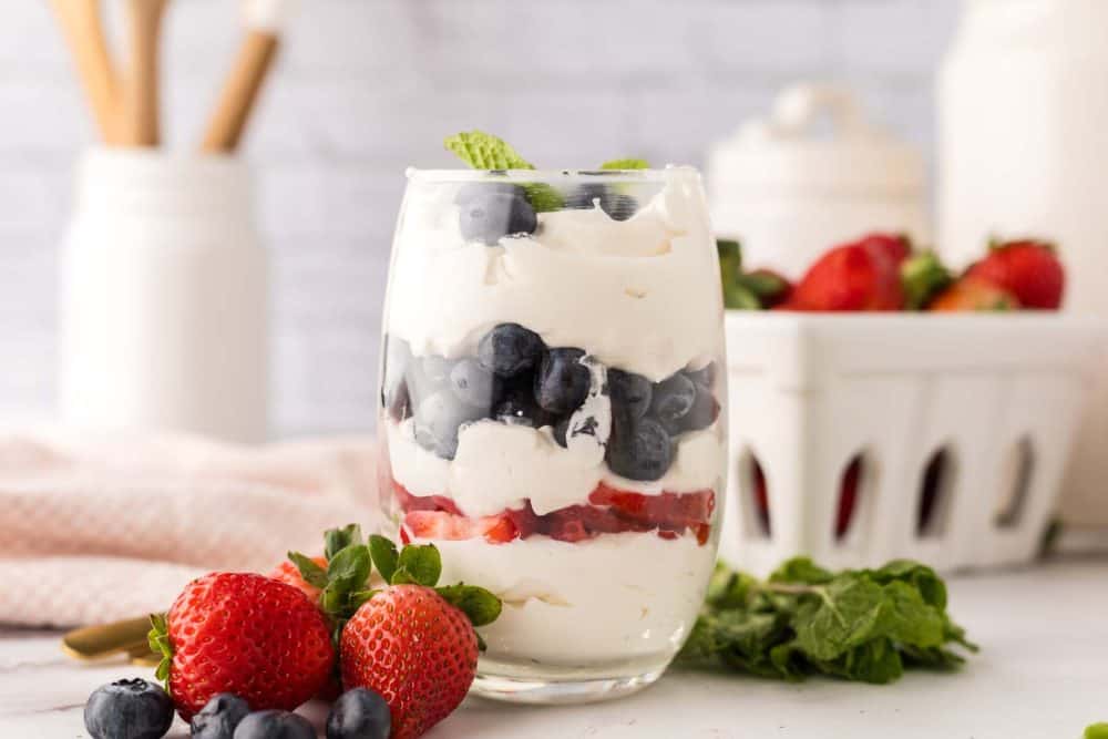 small glass with layered parfait of berries and cream with mint on top.