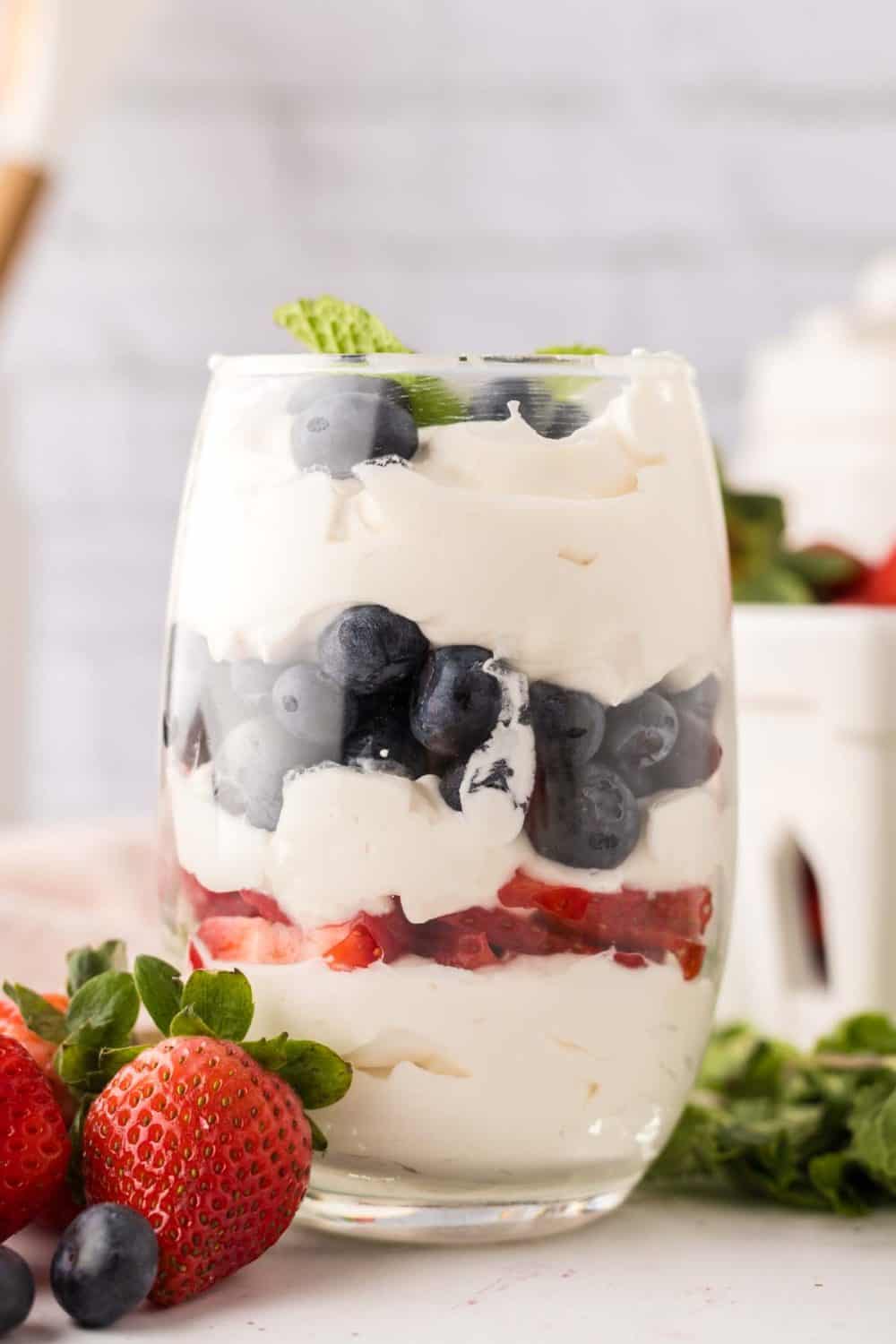 small glass with layered parfait of berries and cream with mint on top.