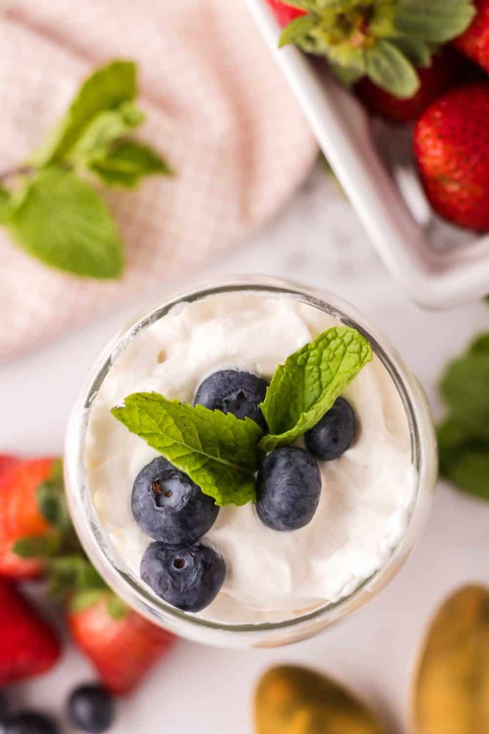 small glass with layered parfait of berries and cream with mint on top.