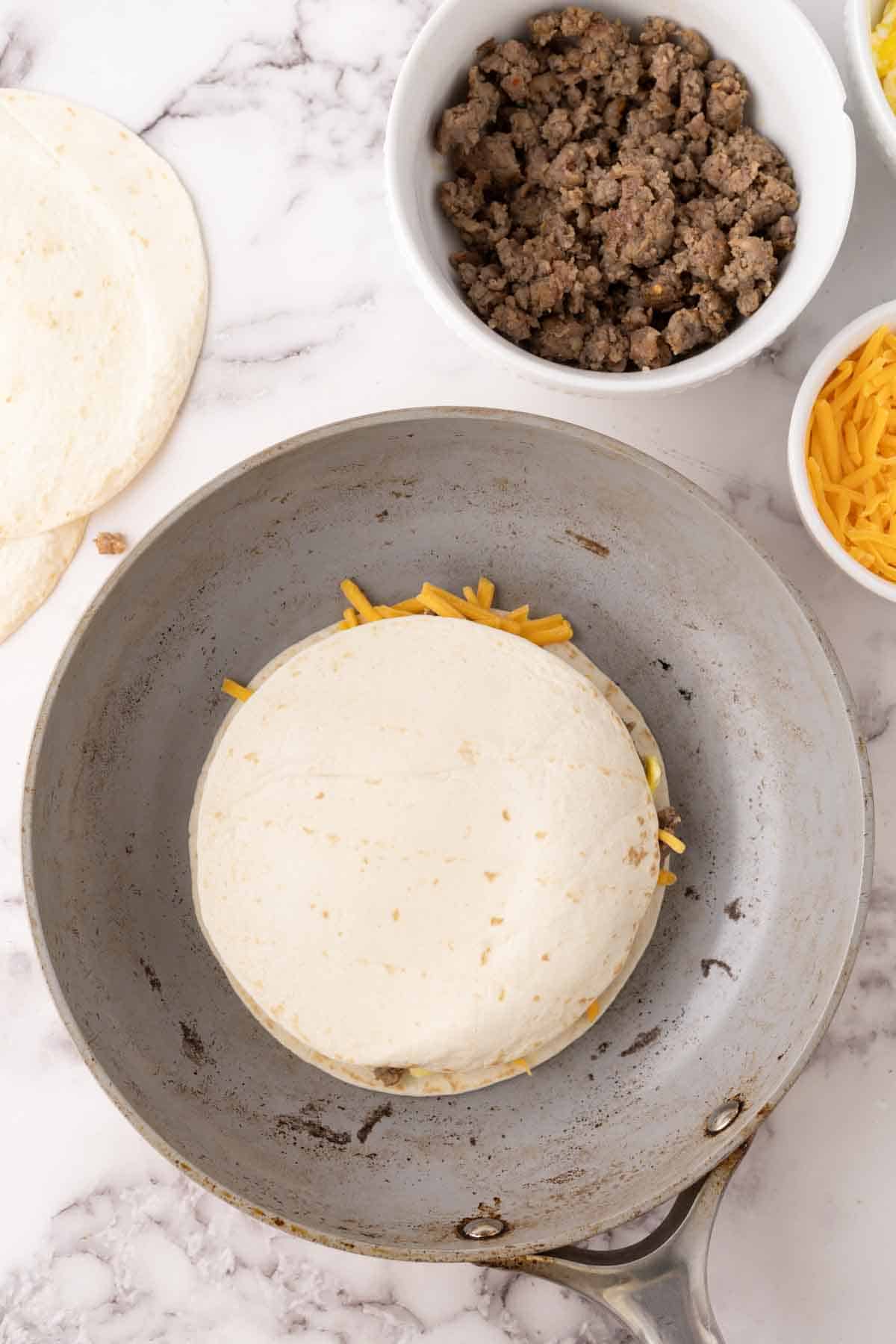 flour tortilla with breakfast quesadilla recipe in progress in the pan.