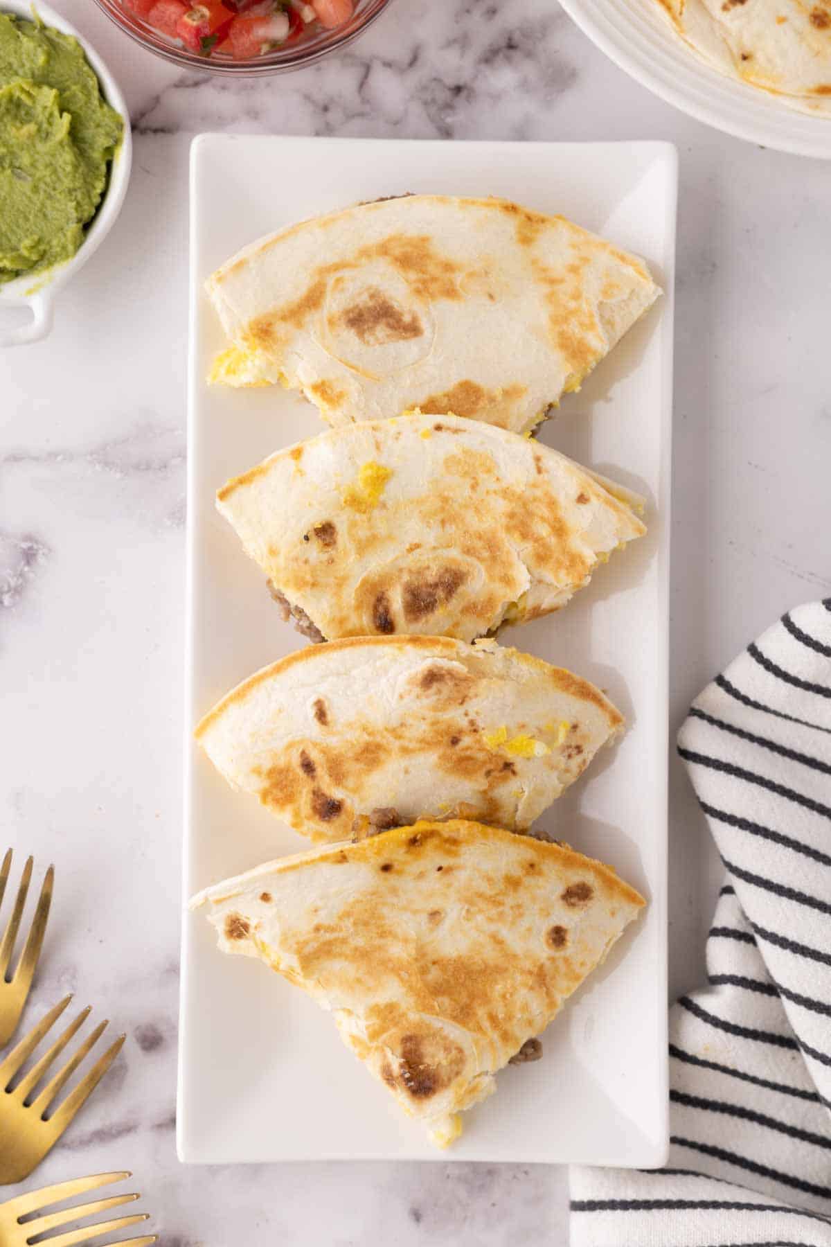 triangles of a flour tortilla with breakfast quesadilla on a rectangle white plate.