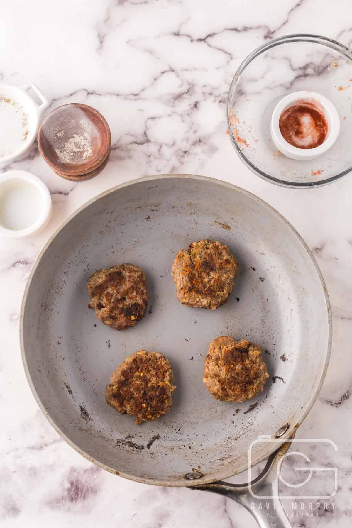 pan with four sausage patties browning.