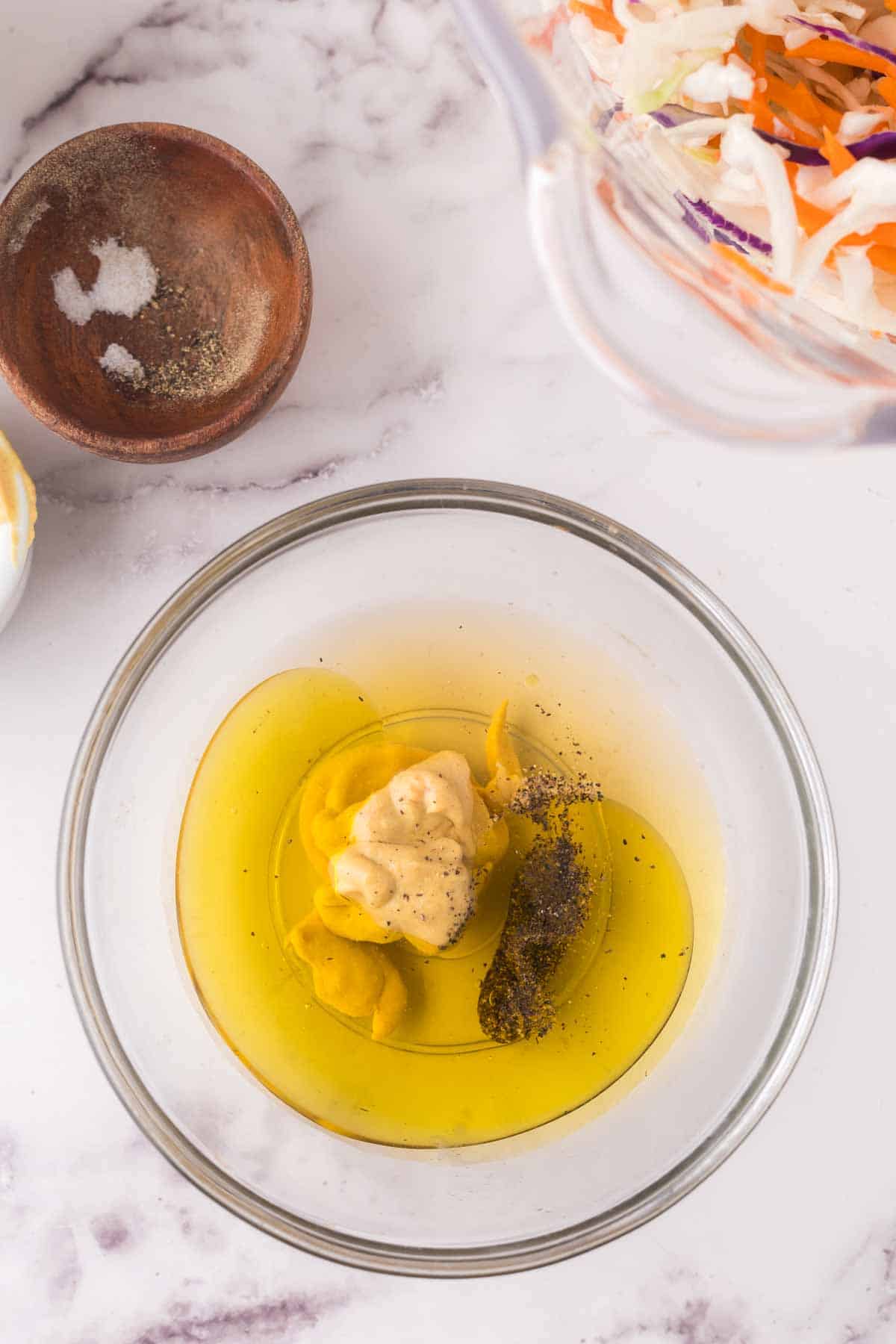 clear mixing bowl with the progress of making cabbage salad dressing.