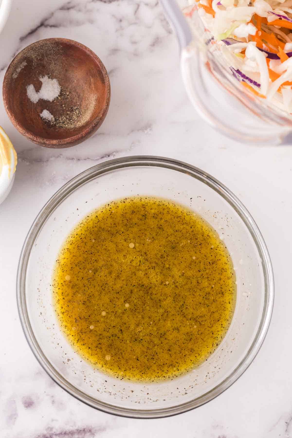 clear mixing bowl with the progress of making cabbage salad dressing.