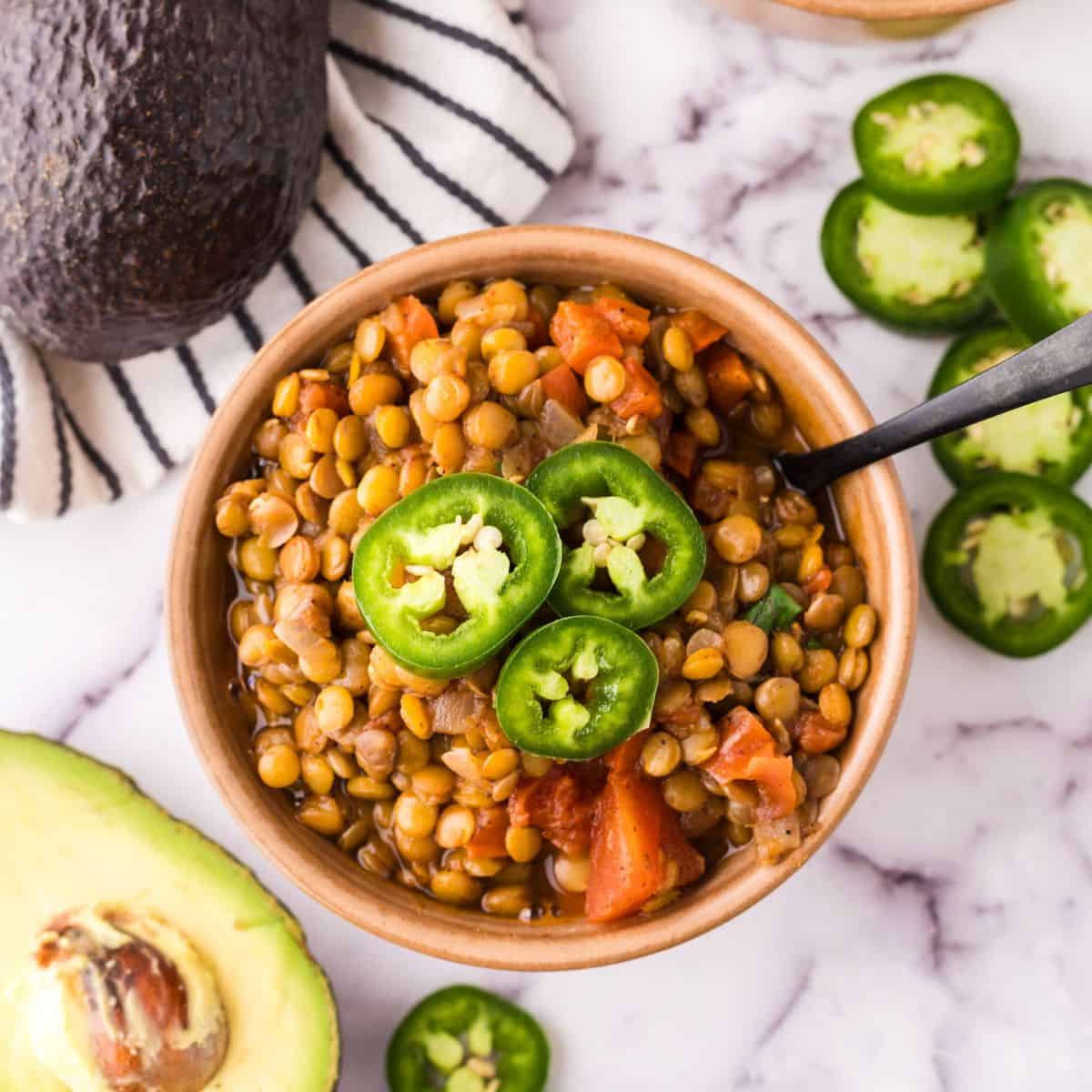 bowl of lentil chili with fresh sliced jalapeño on top and a spoon inside.