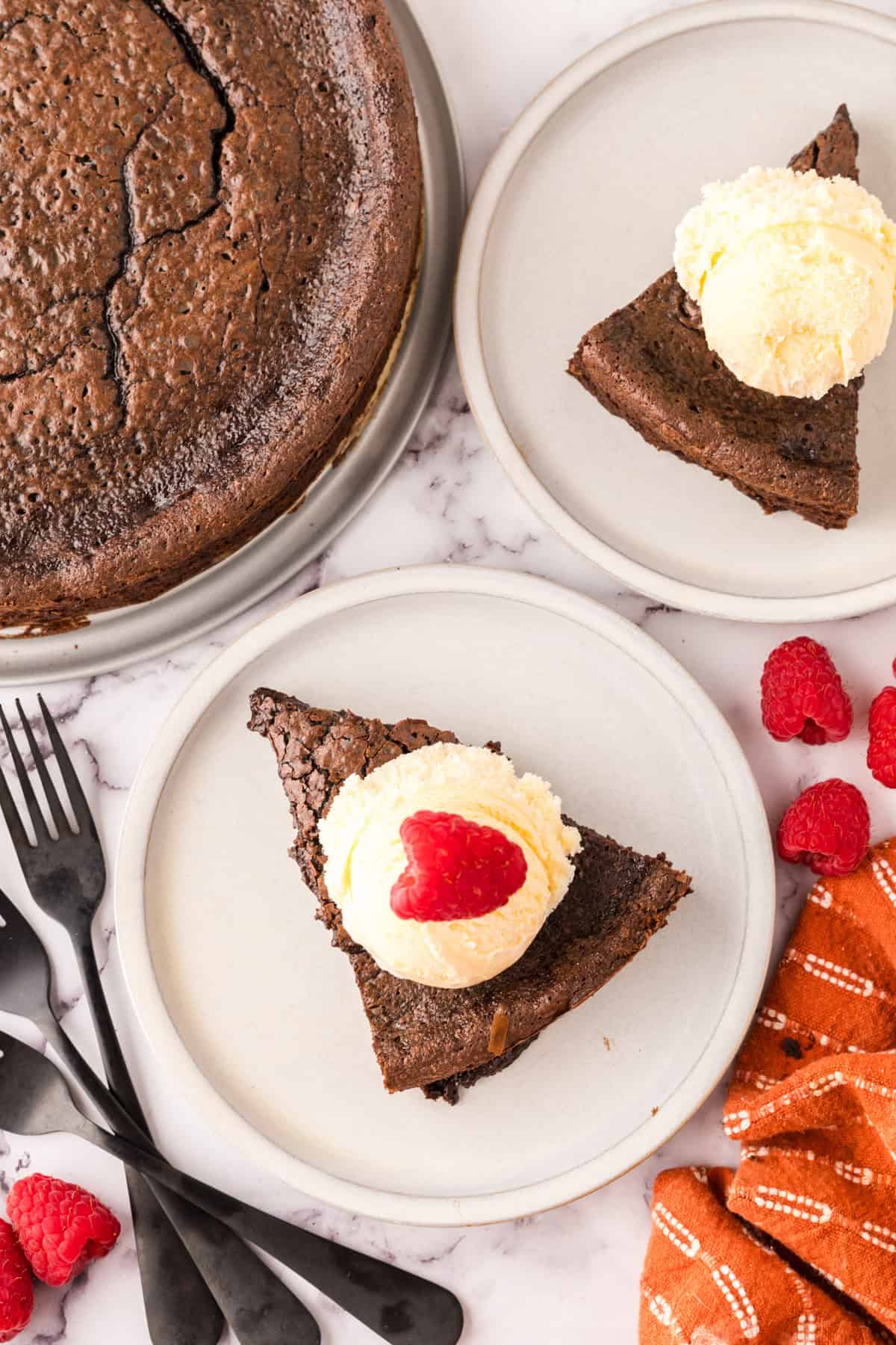 flourless chocolate cake on a round plate with vanilla ice cream and a raspberry on top.