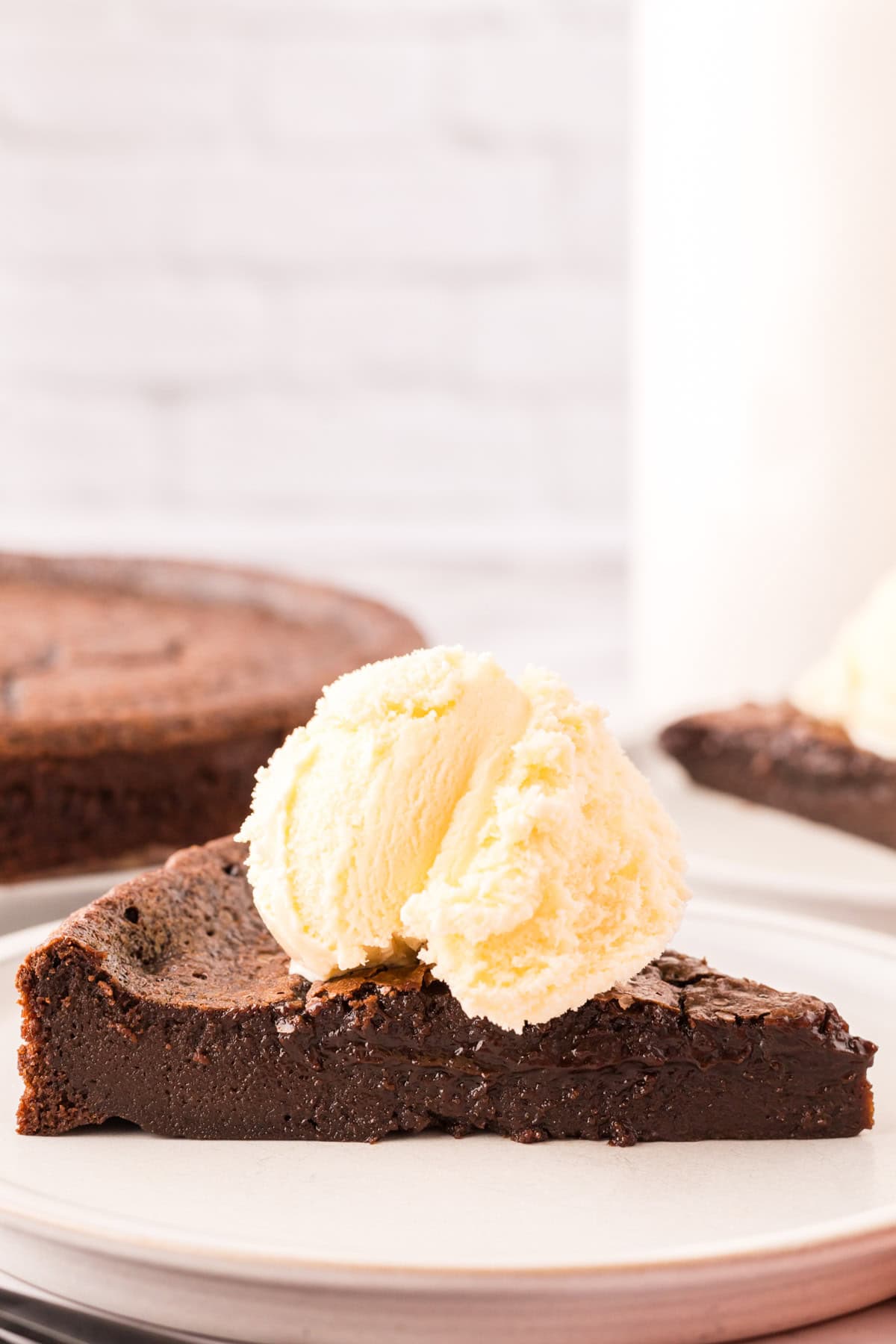 flourless chocolate cake on a round plate with vanilla ice cream and a raspberry on top.