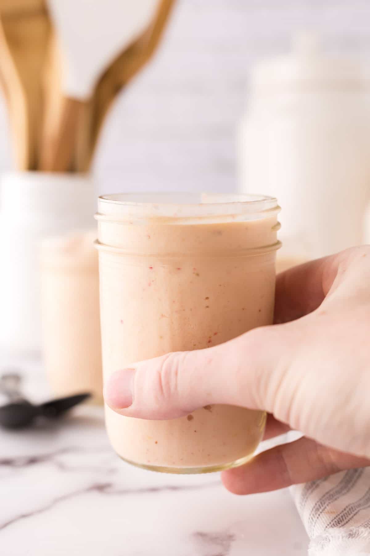 POV hand holding a small mason jar with a smoothie.