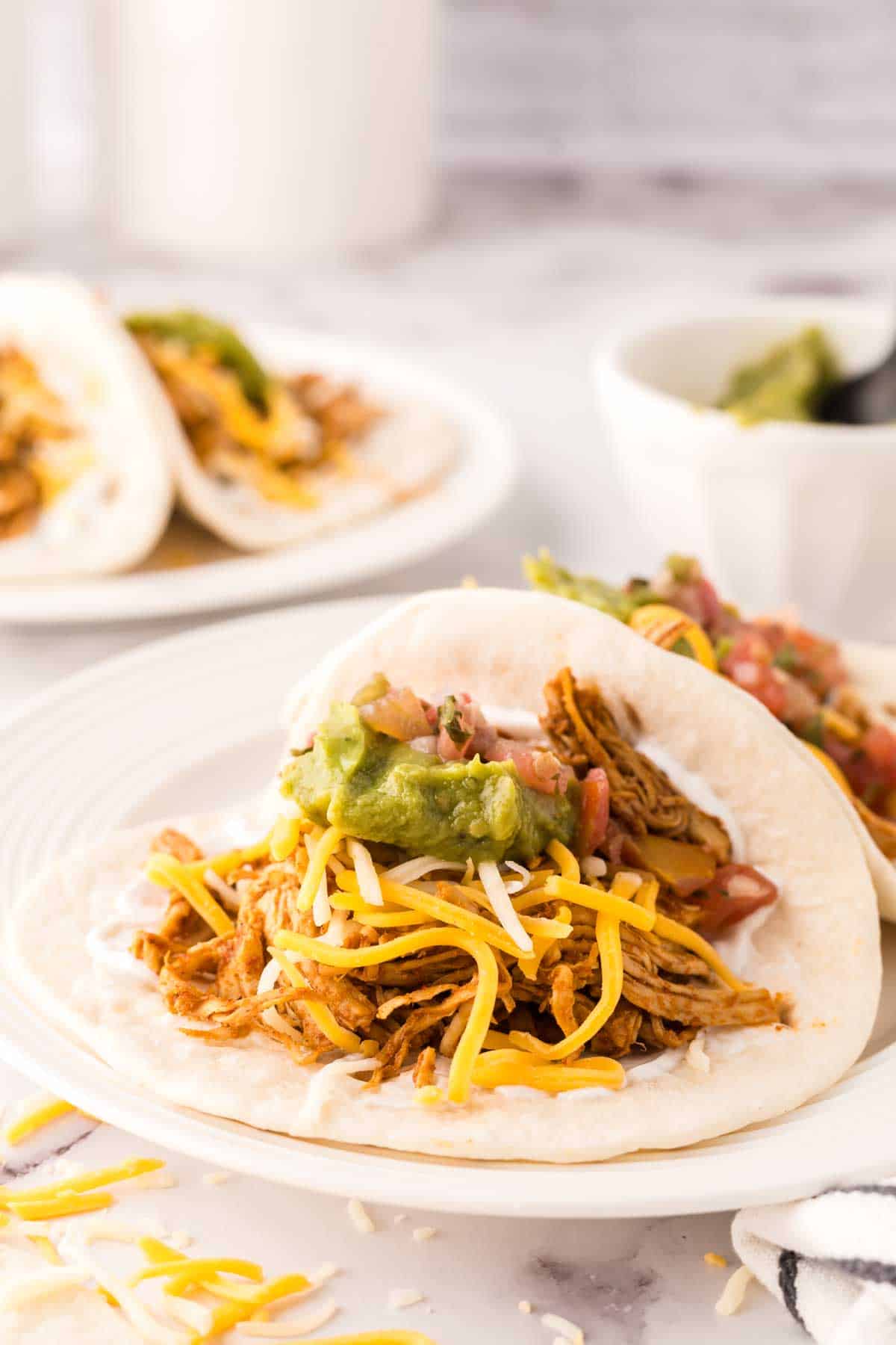 two shredded chicken tacos recipe on a round white plate with guacamole on top.