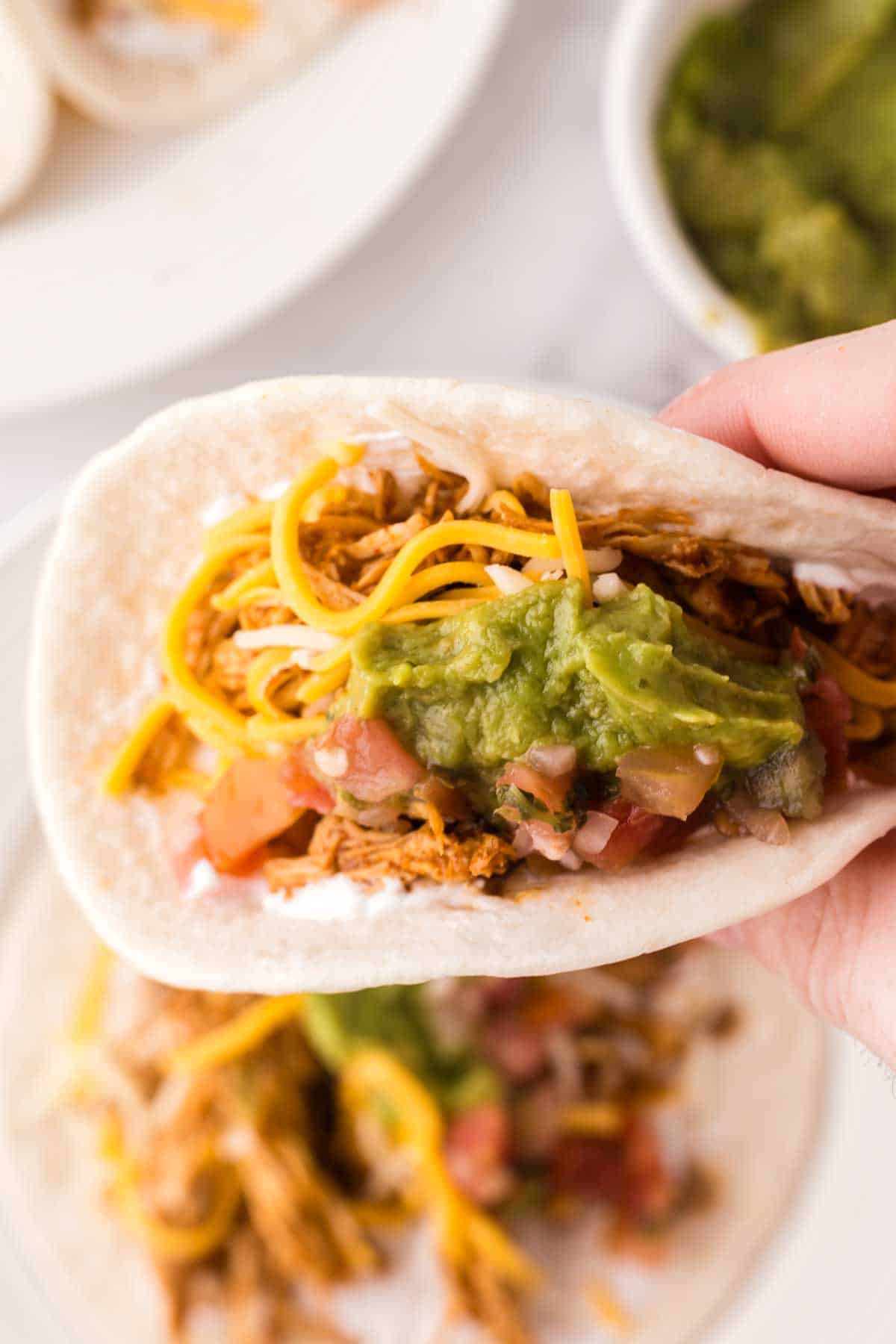 two shredded chicken tacos recipe on a round white plate with guacamole on top.