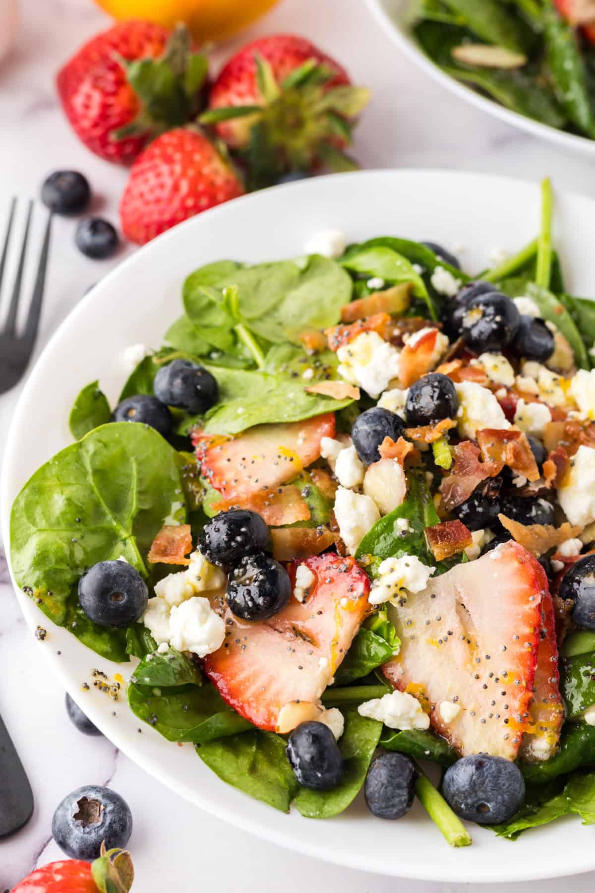 spinach and berry salad on a round white plate with black forks to the side.