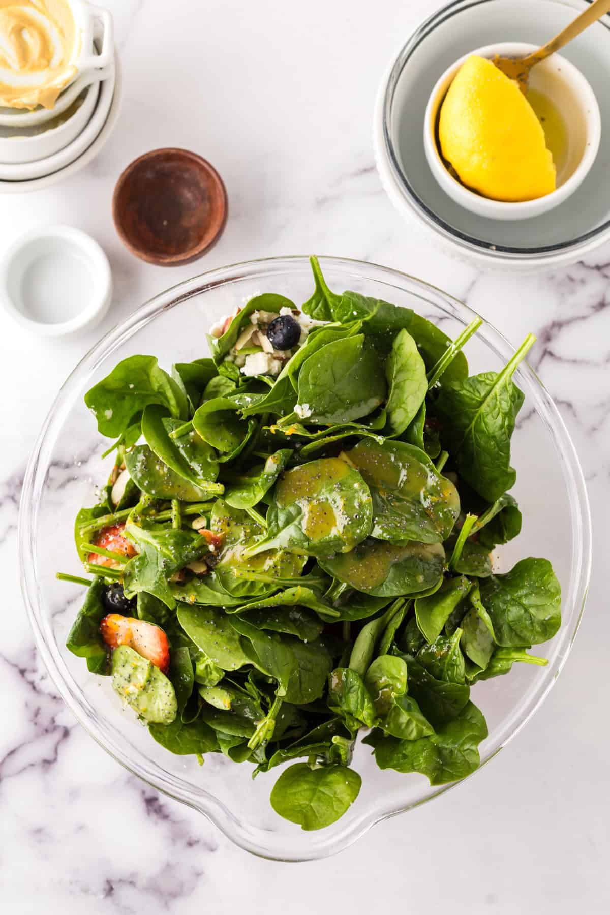 clear mixing bowl in the process of making a spinach berry salad.