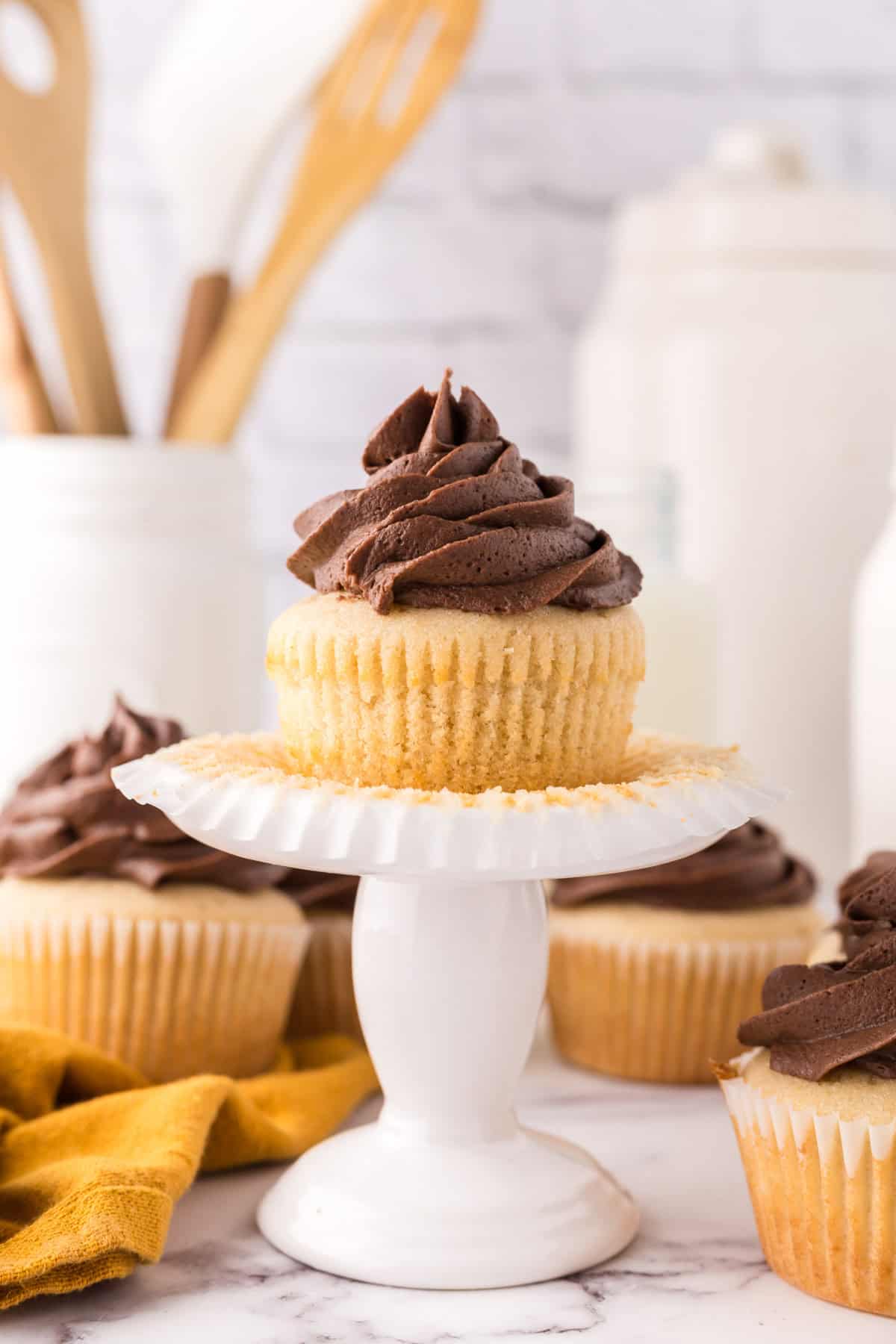 vanilla cupcakes with chocolate frosting on an ornate stand.