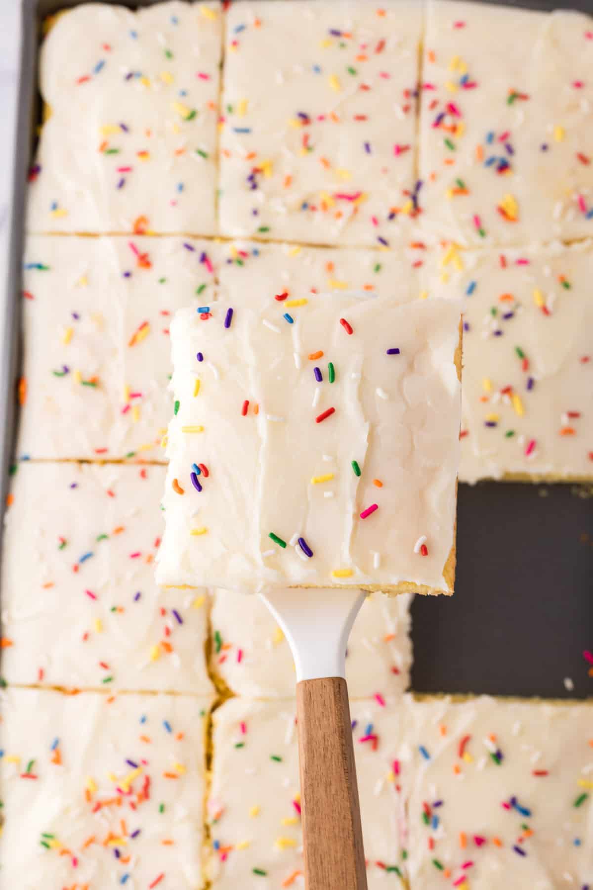 one square serving of vanilla sheet cake over the pan on a spatula.