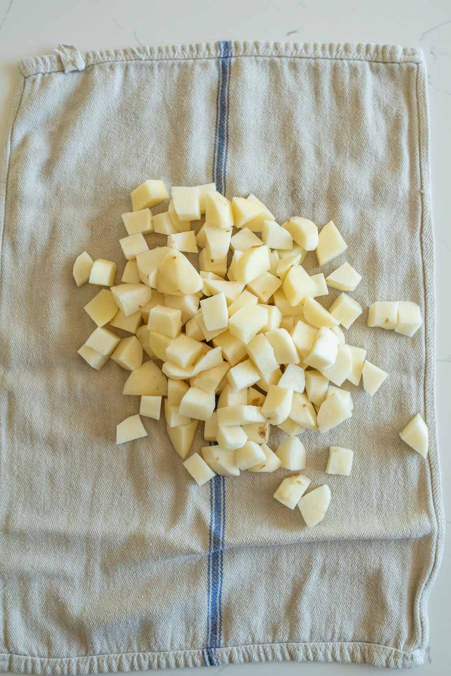 Raw potato cubes on a light grey towel after being dried.