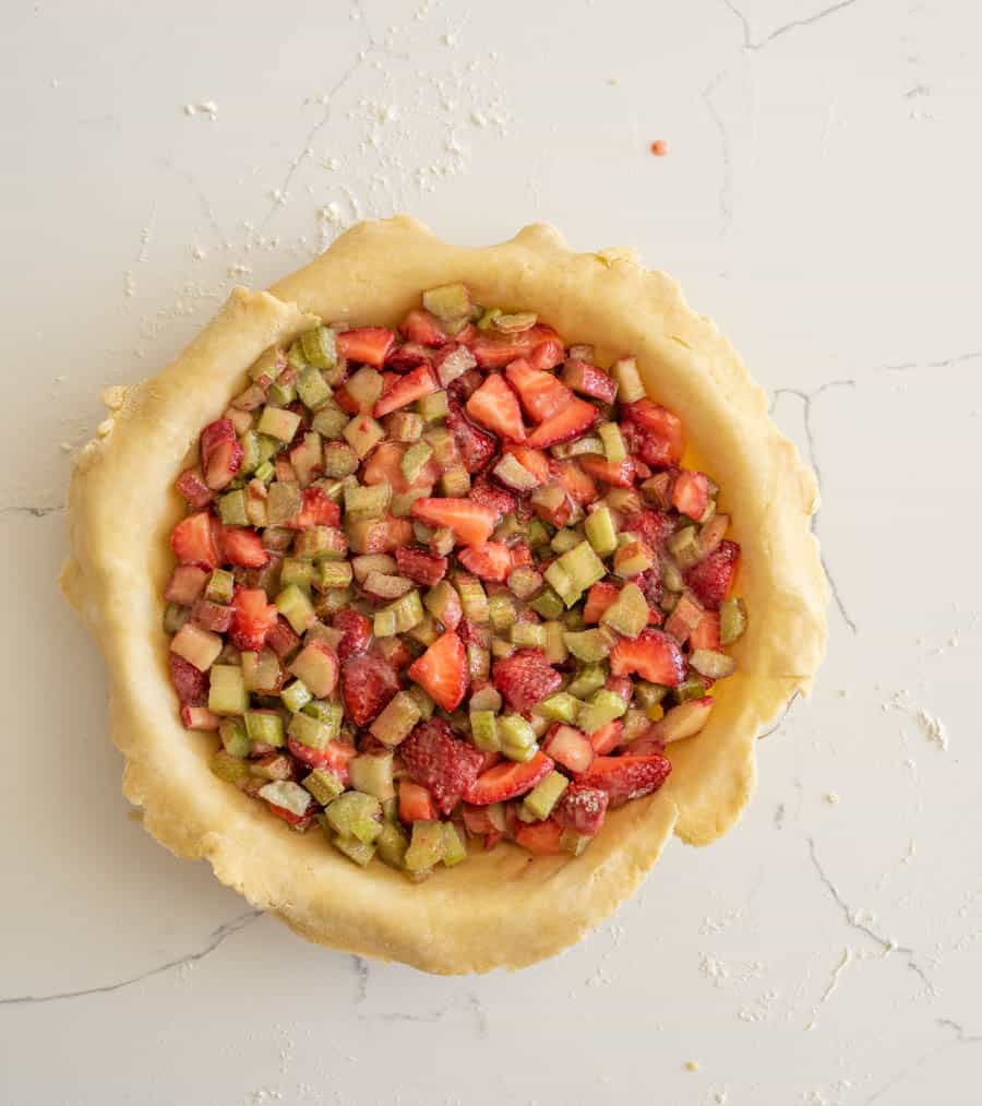 Pie filling of rhubarb and strawberries in the pie crust on a white counter.