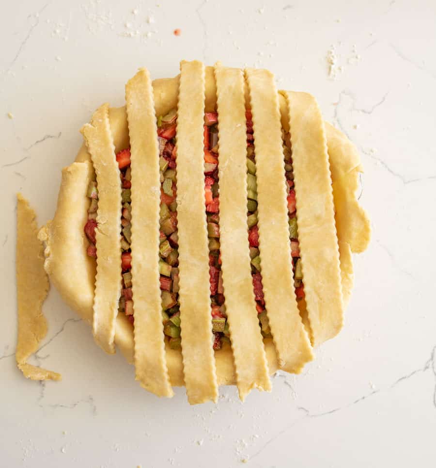 Six pie crust strips laid across the top of the pie with about one-half inch between them on a white counter.