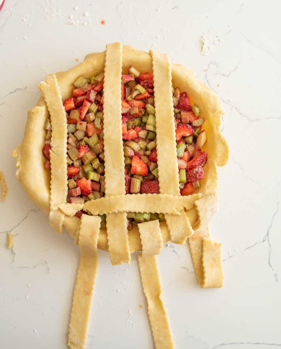 A strip of pie crust place perpendicular on the three strips resting on top of the pie.