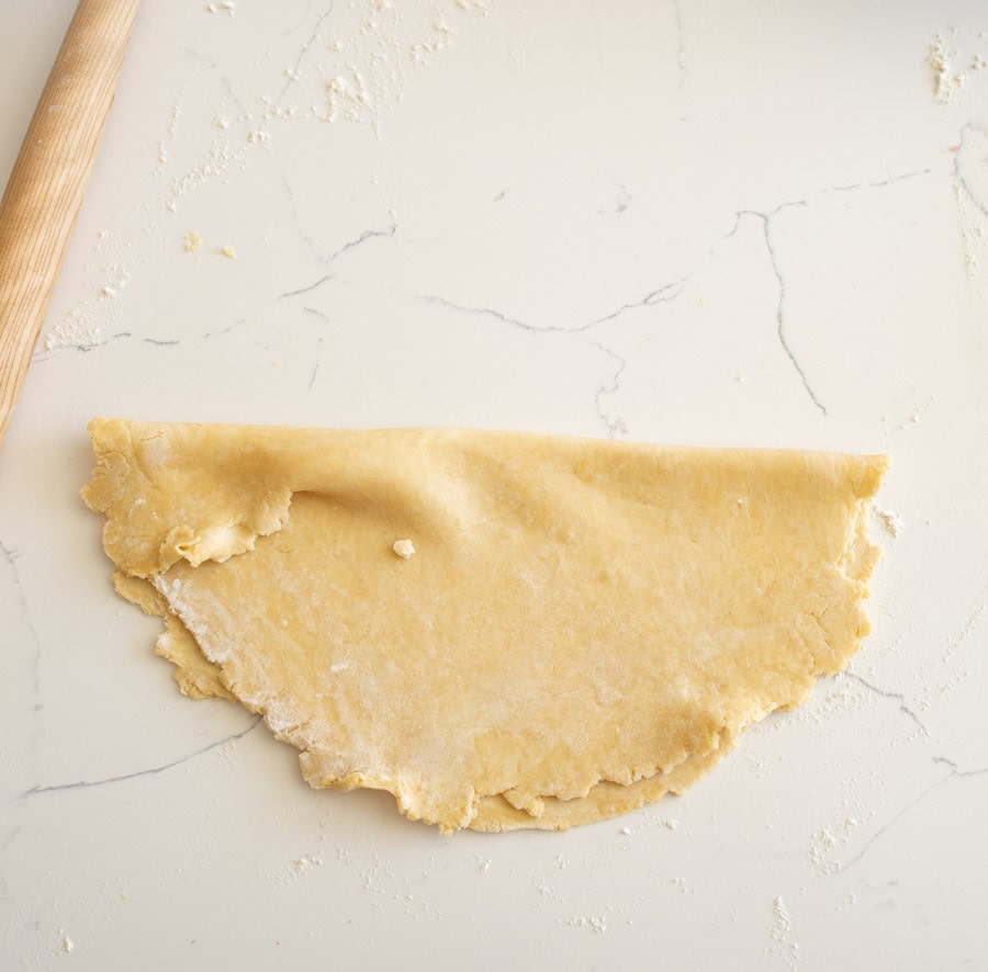 A pie crust folded in half into a semi-circle on a white counter.
