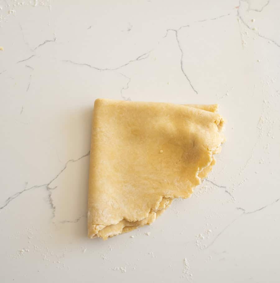 A pie crust folded in half twice so that it's in the shape of a quarter of a circle on a white counter.