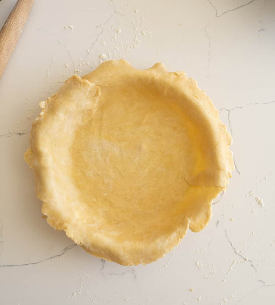 The pie crust unfolded into the clear glass pie plate on a white counter.