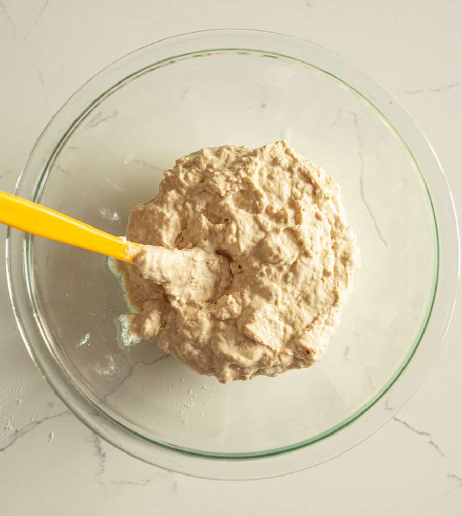 Ingredients mixed together in a clear glass bowl with a yellow spatula before the batter rests.