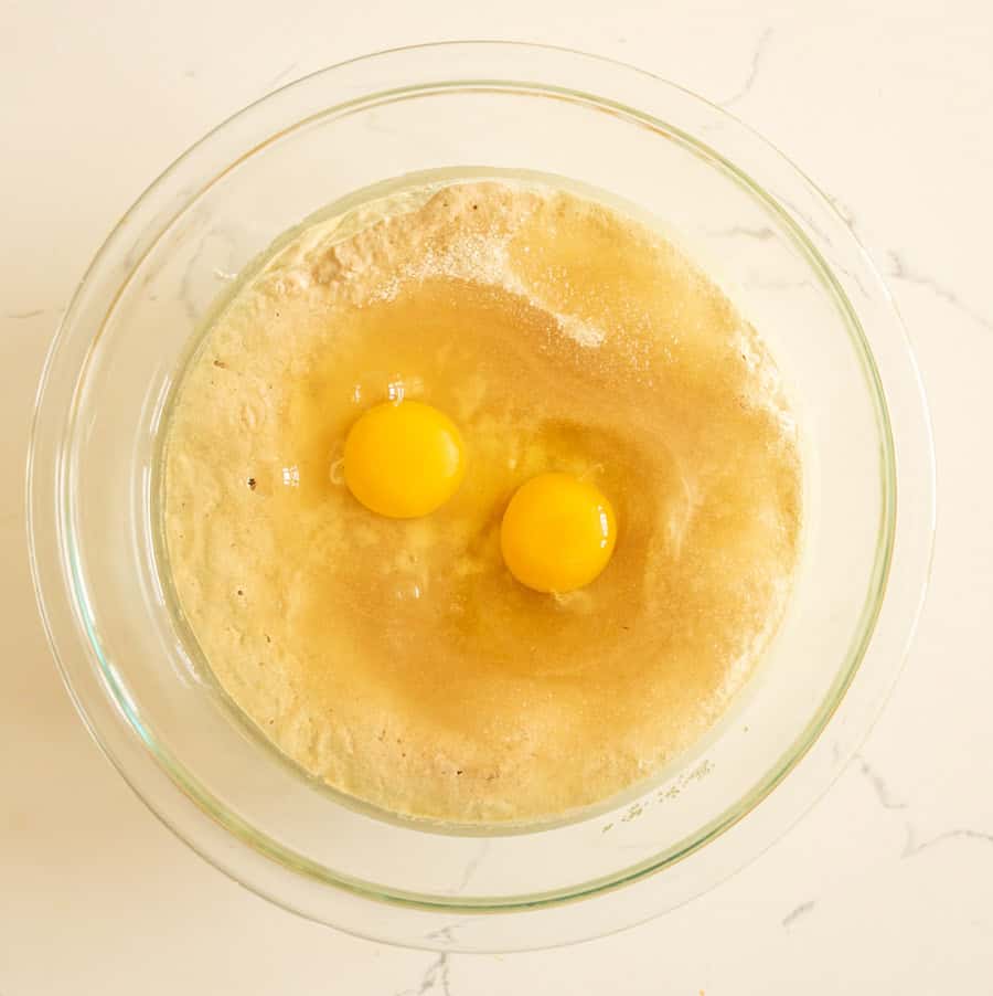 Sourdough muffin batter in a clear glass bowl with two eggs added.
