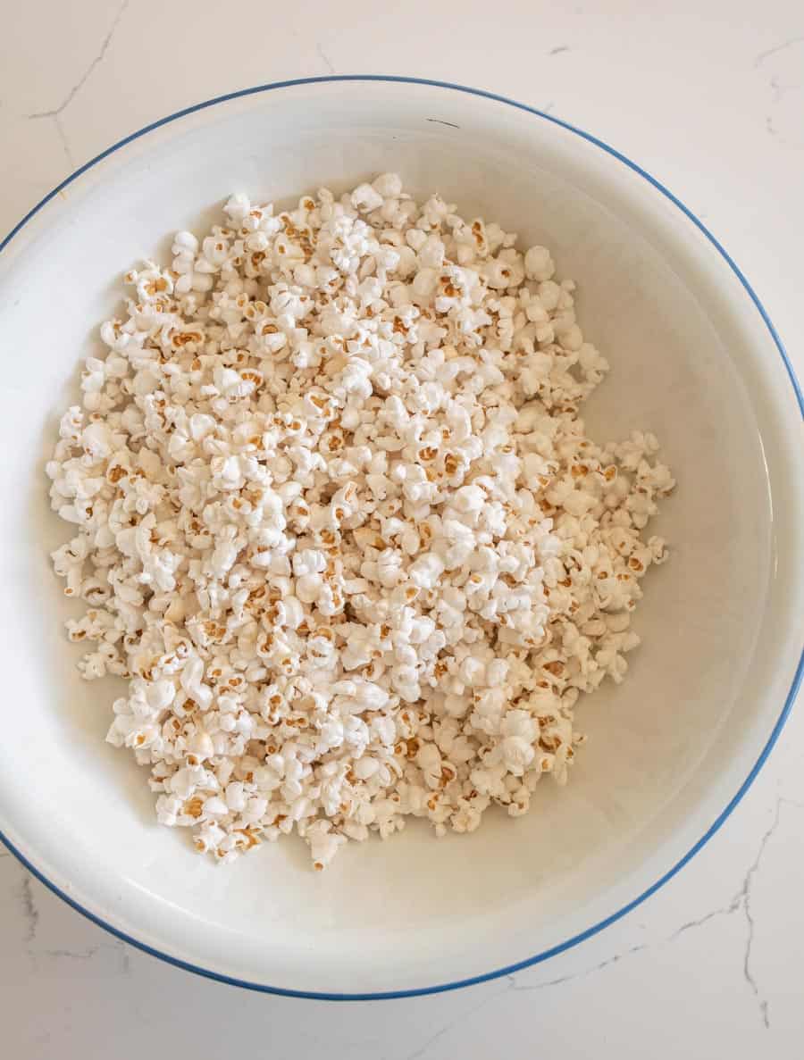 Large white enamel bowl with a blue rim with popped popcorn.