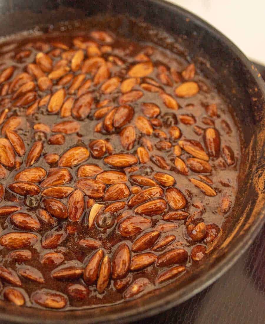 Almonds cooking in the sugary sauce in a cast iron pan.