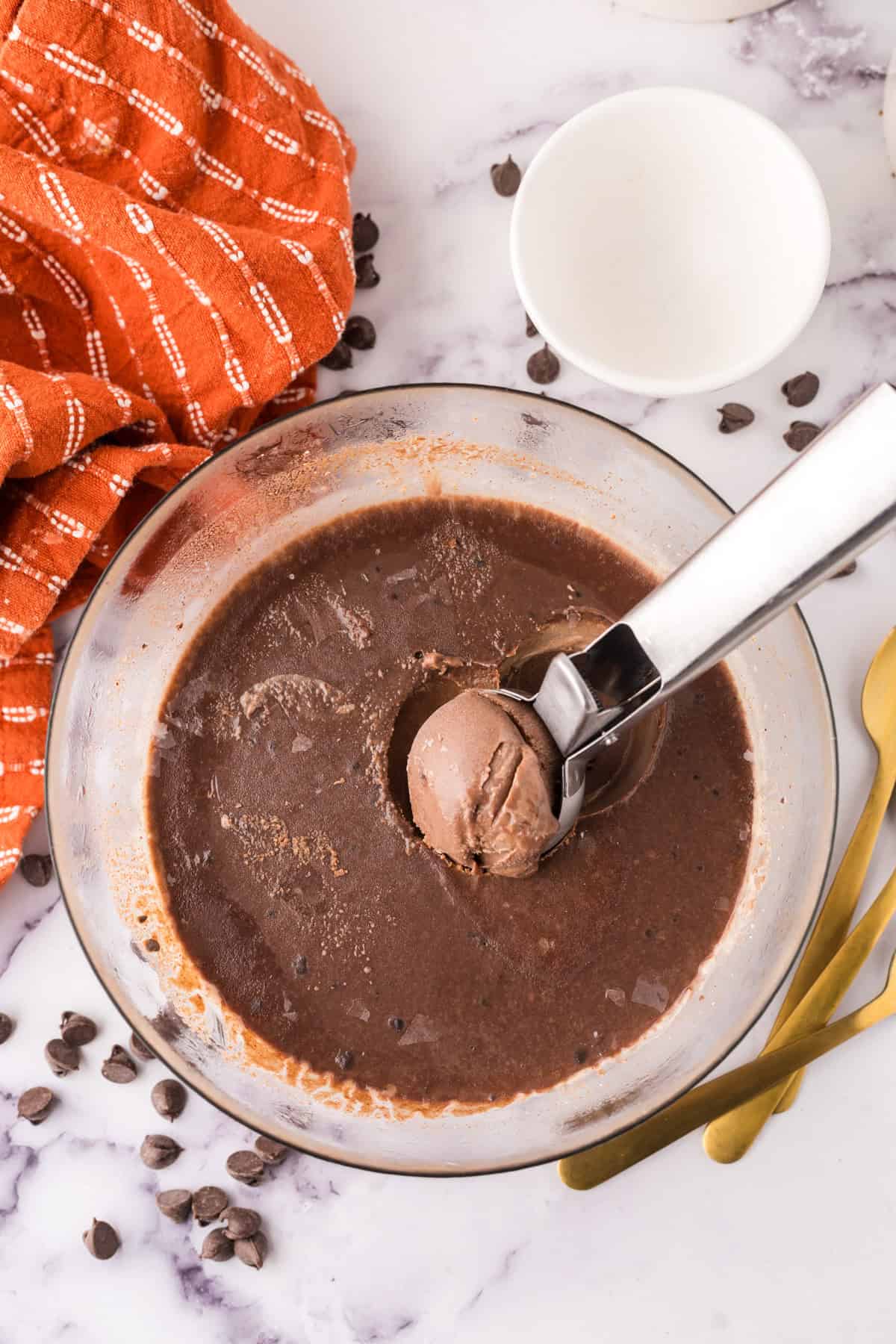 clear mixing bowl in the process of making chocolate truffle ice cream and a scoop.