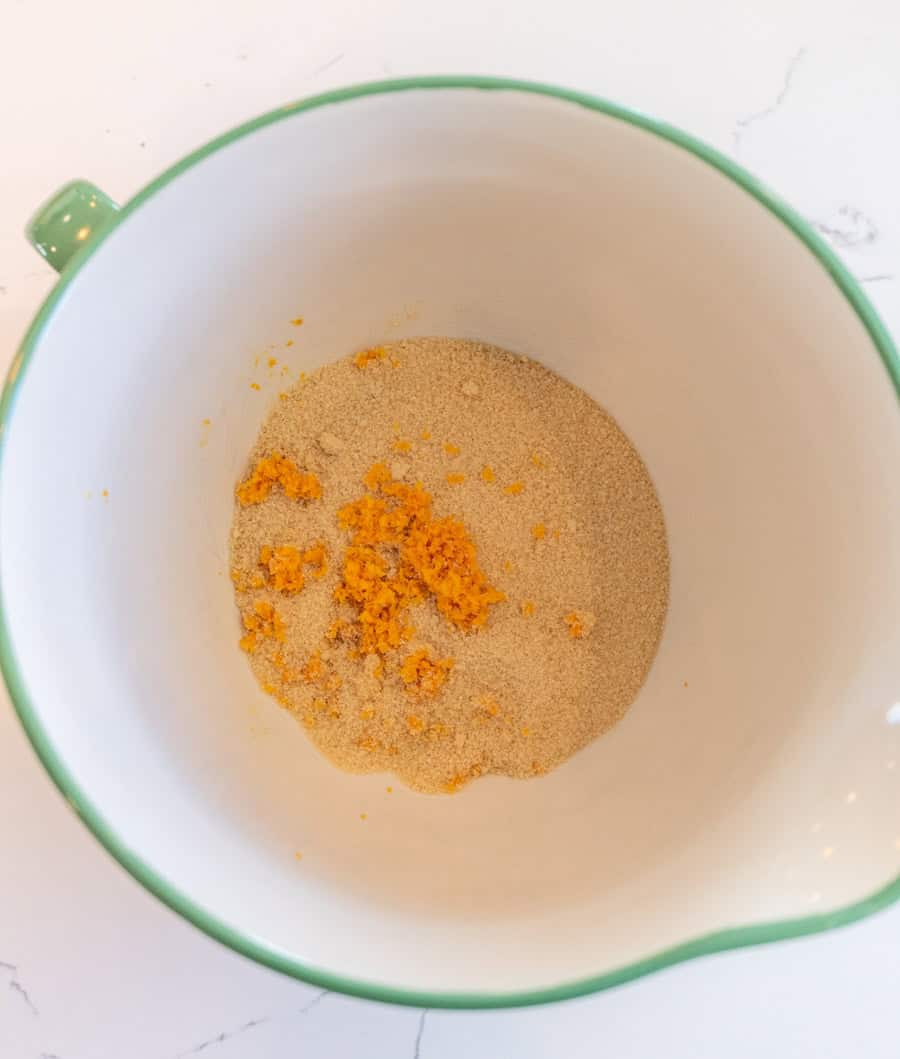 Sugar and orange zest in a white bowl with a green rim.