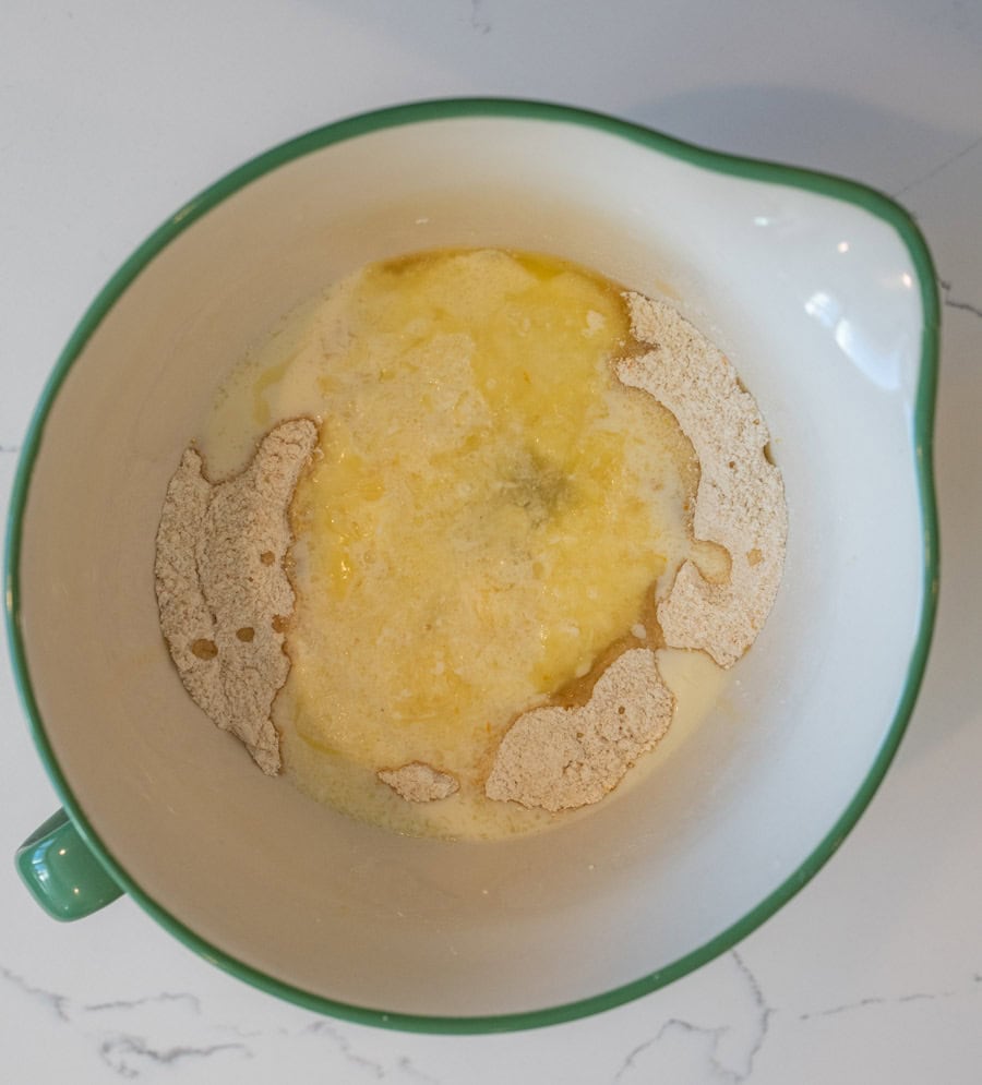 The wet and dry ingredients for cranberry orange bread about to be combined in a white mixing bowl with a green rim.