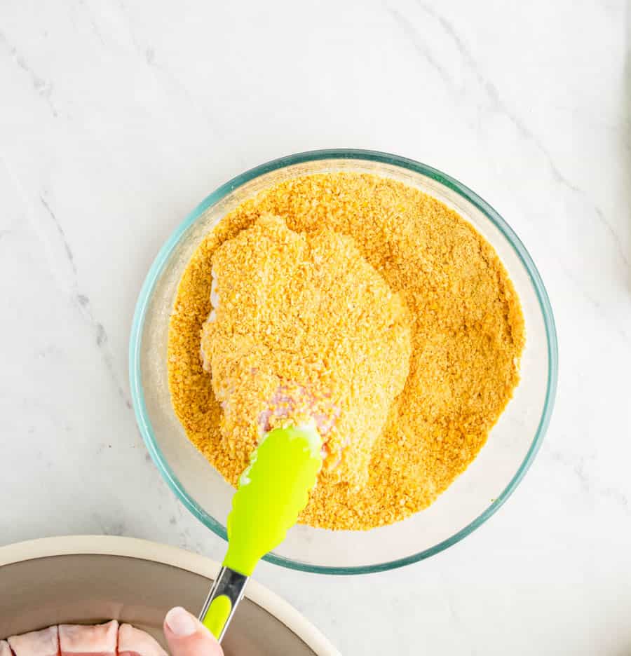 Pork chop being coated with the corn flake crumbs.