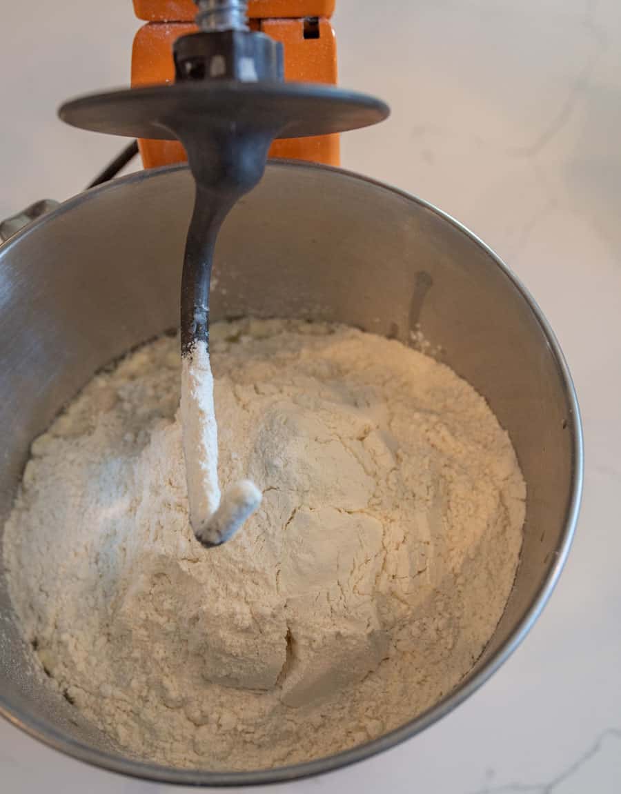 Stand mixer with a dough hook on and ingredients for extra soft white bread in the mixing bowl.