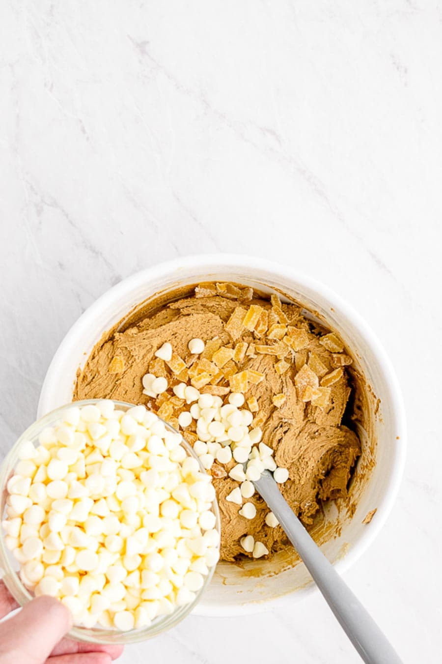 White chocolate chips being added to the white mixing bowl in the process of making gingerbread blondie batter.
