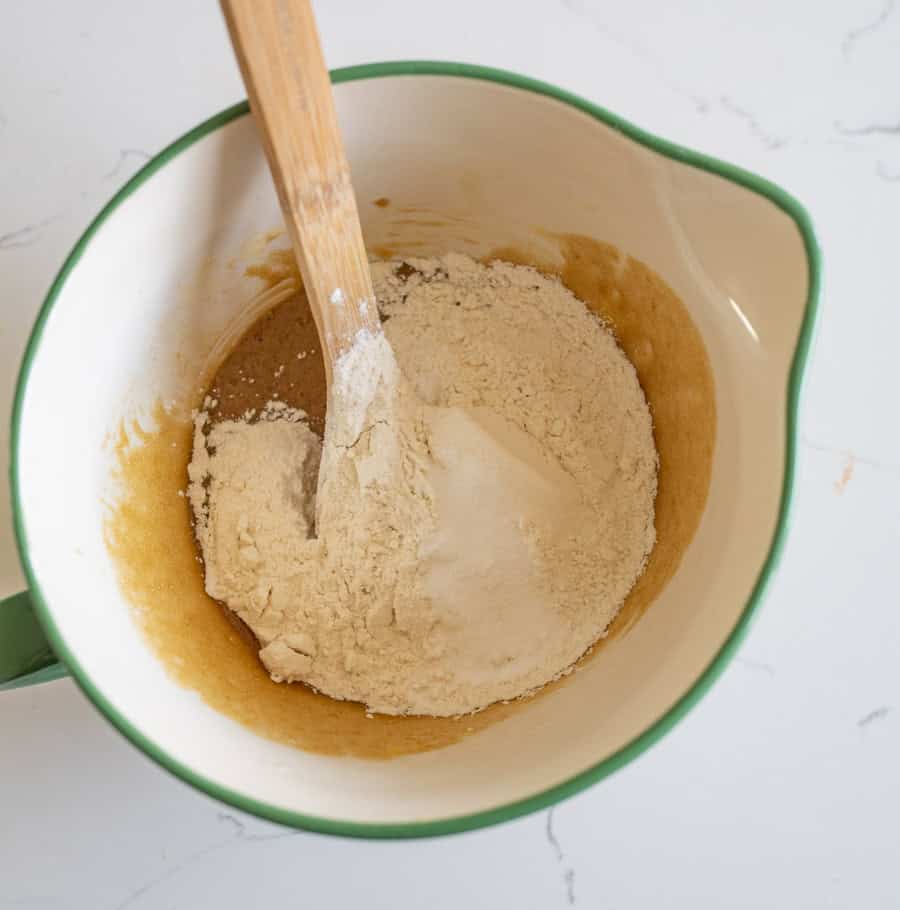 Dry ingredients added to the Halloween candy cookie bar dough in a white bowl with a green rim on a white counter.