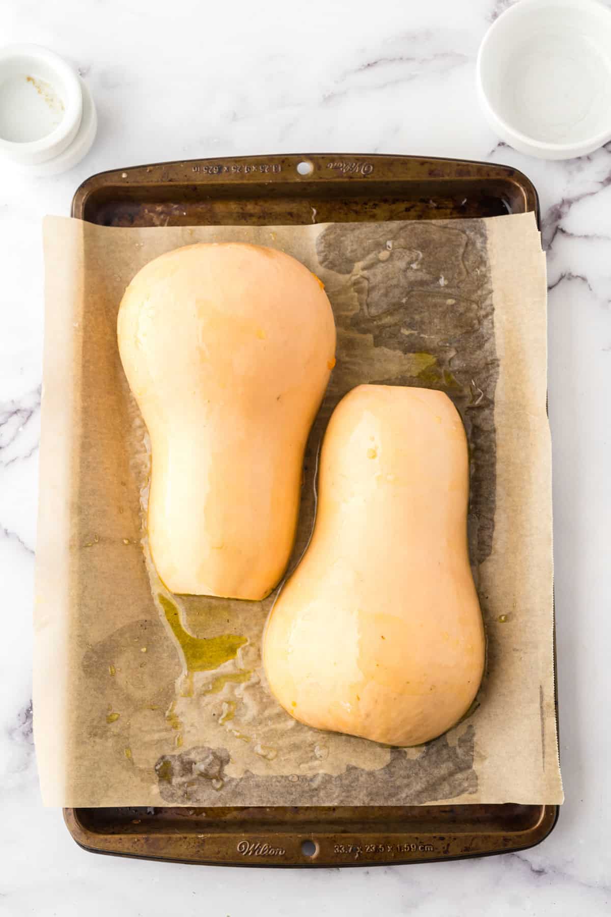 how to bake butternut squash showing the halved squash on parchment over a baking sheet upside down.