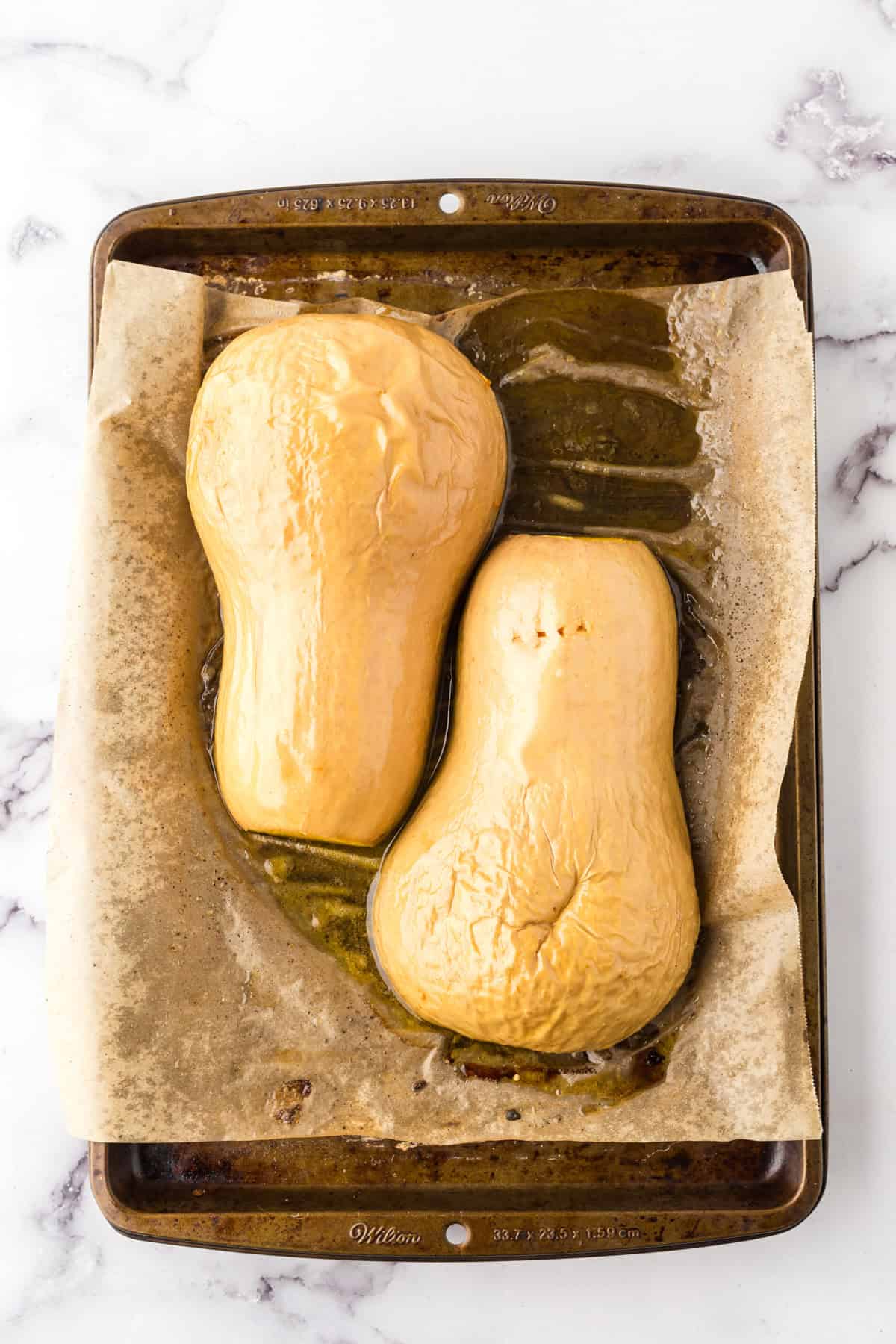 how to bake butternut squash showing the halved squash on parchment over a baking sheet.