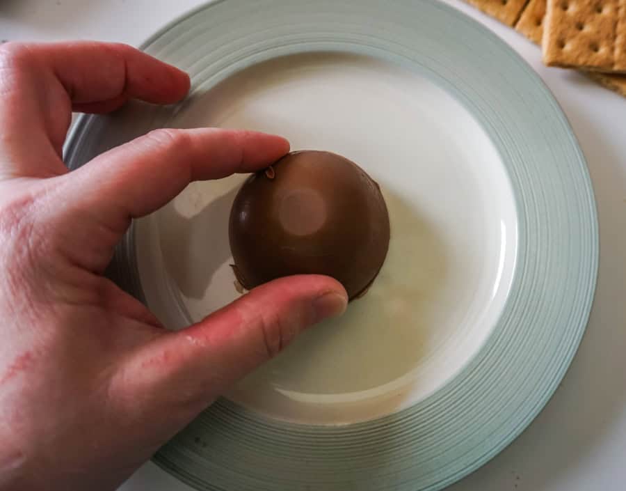 A hand rubbing half of a chocolate bomb on a warm plate.