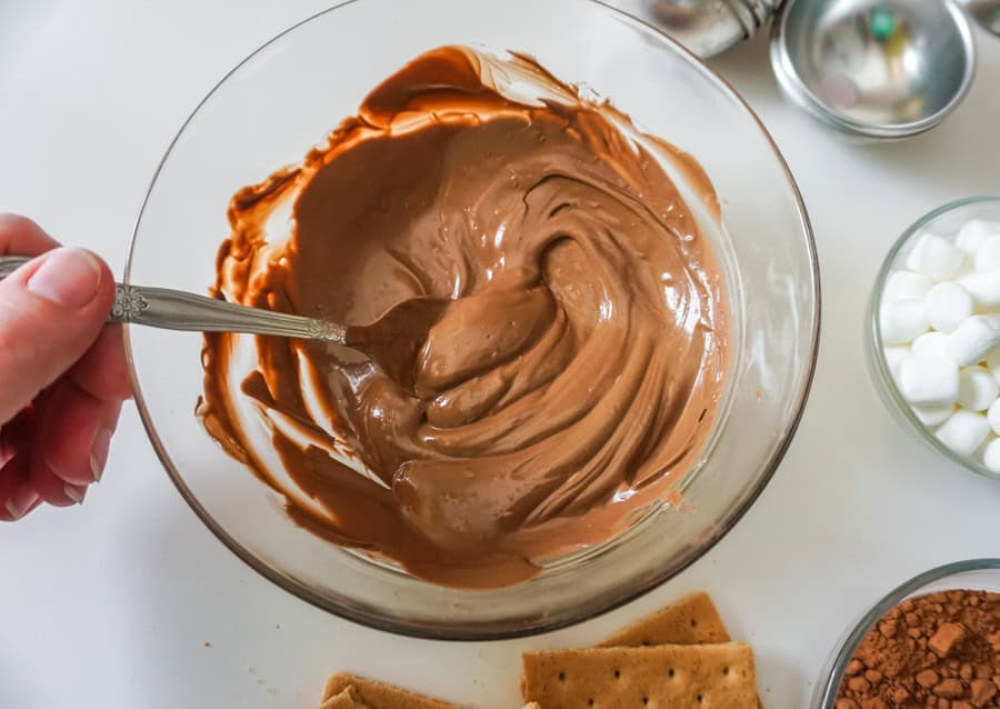Melted chocolate candy melts in a clear glass bowl with a spoon.