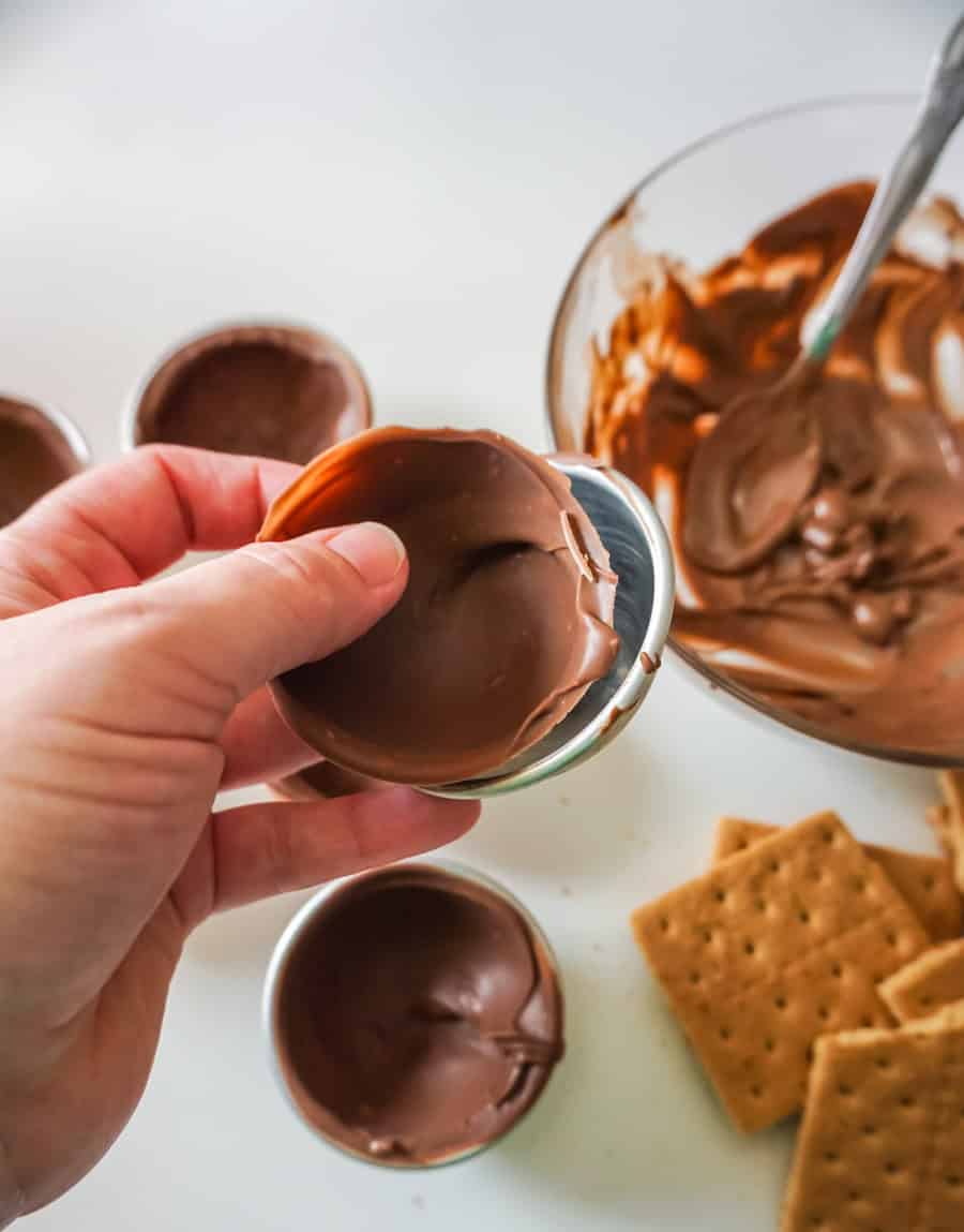 A hand removing half of a hot chocolate bomb from a stainless steel mold.